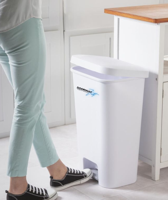 Woman opening white trash can with foot in kitchen.