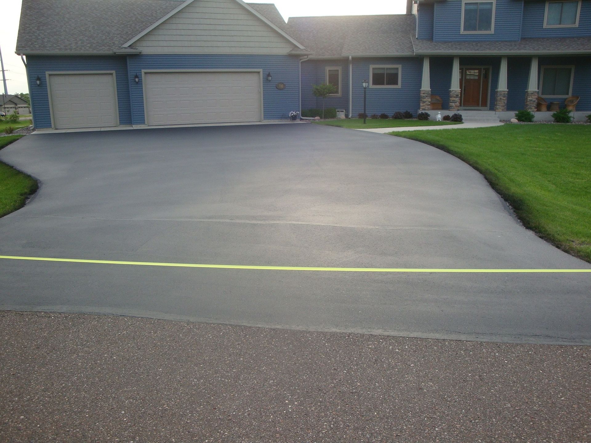 Black asphalt driveway in front of a blue house with a two-car garage and green lawn.