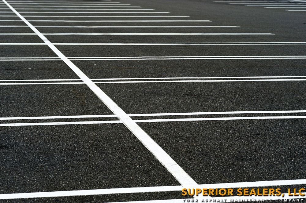 Parking lot asphalt with white painted parking space lines. A large white line intersects other lines.