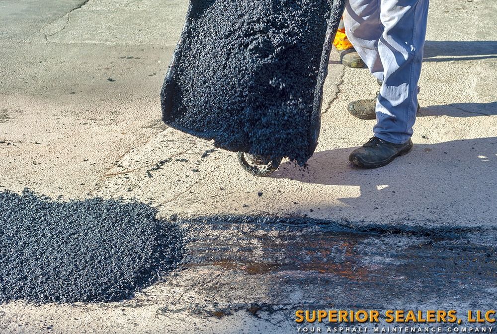 Person patching a road with asphalt, demonstrating the repair process.  A large chunk of asphalt is being placed.