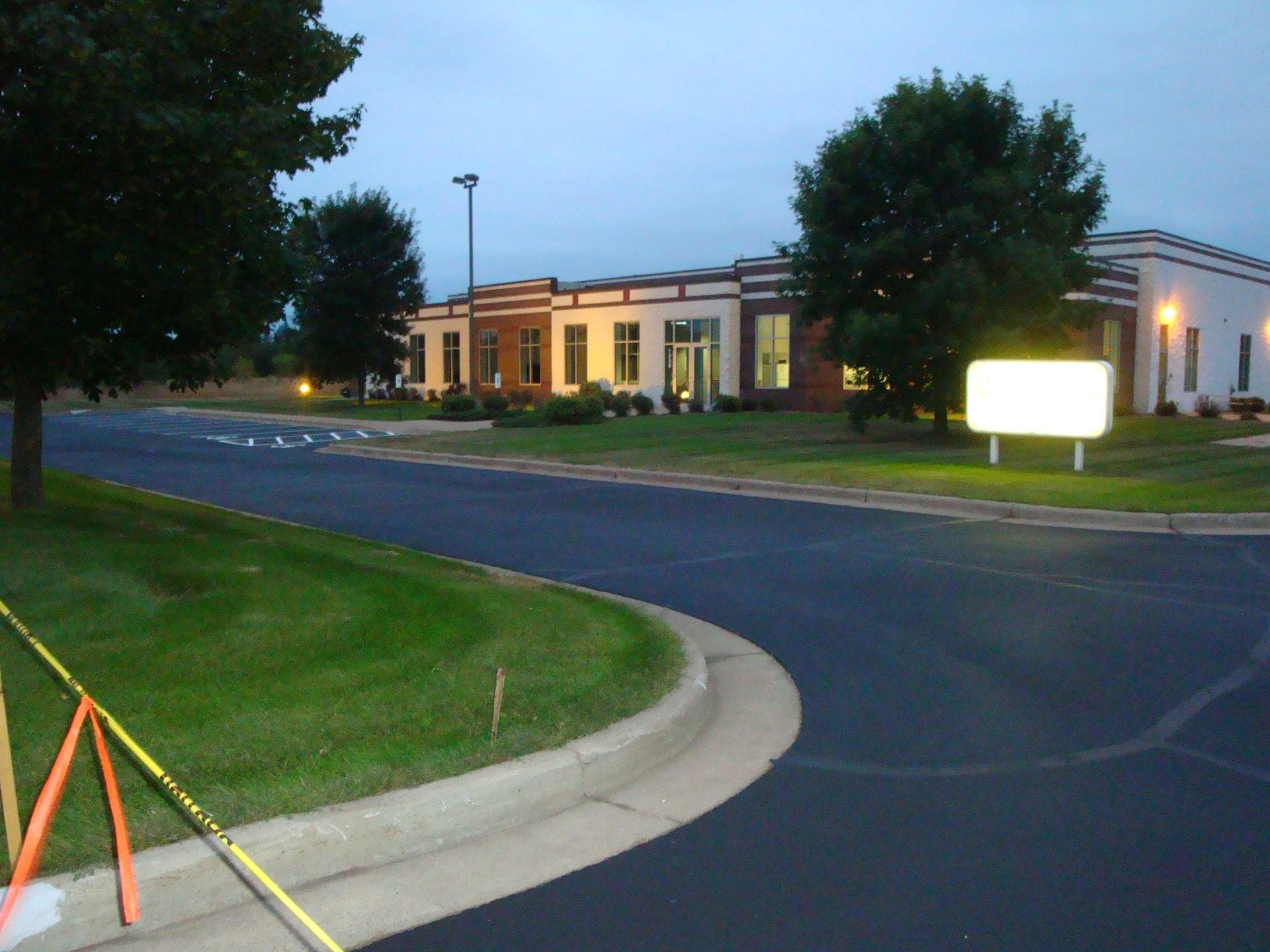 A building at dusk with a lit sign, dark asphalt road, and green grass.