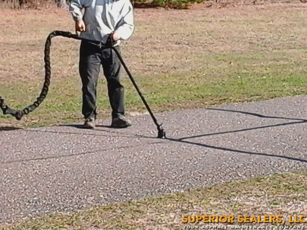 Man using a crack sealing machine on an asphalt surface. The machine is black, and the asphalt has gray tones.