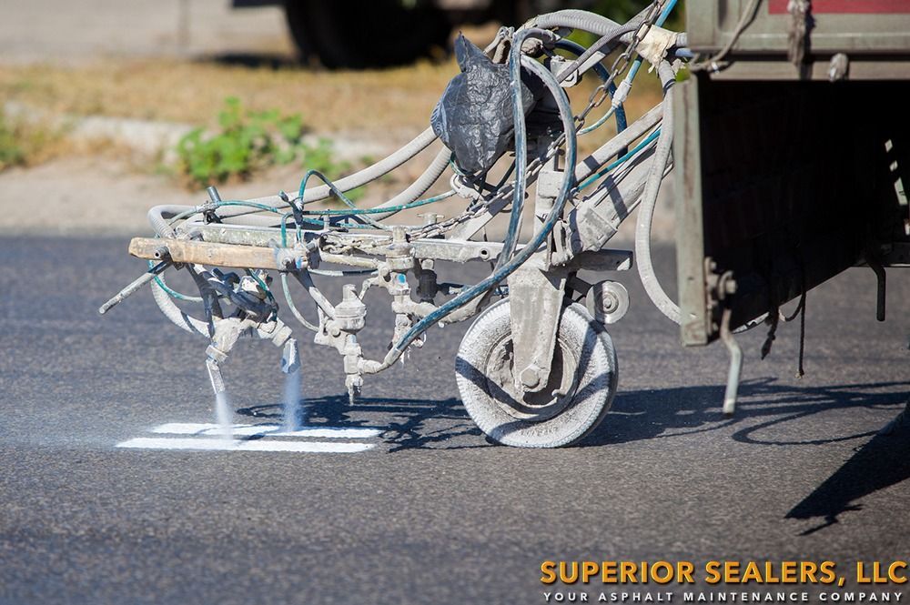 A road-marking machine spraying white paint onto asphalt, creating a parking space line.