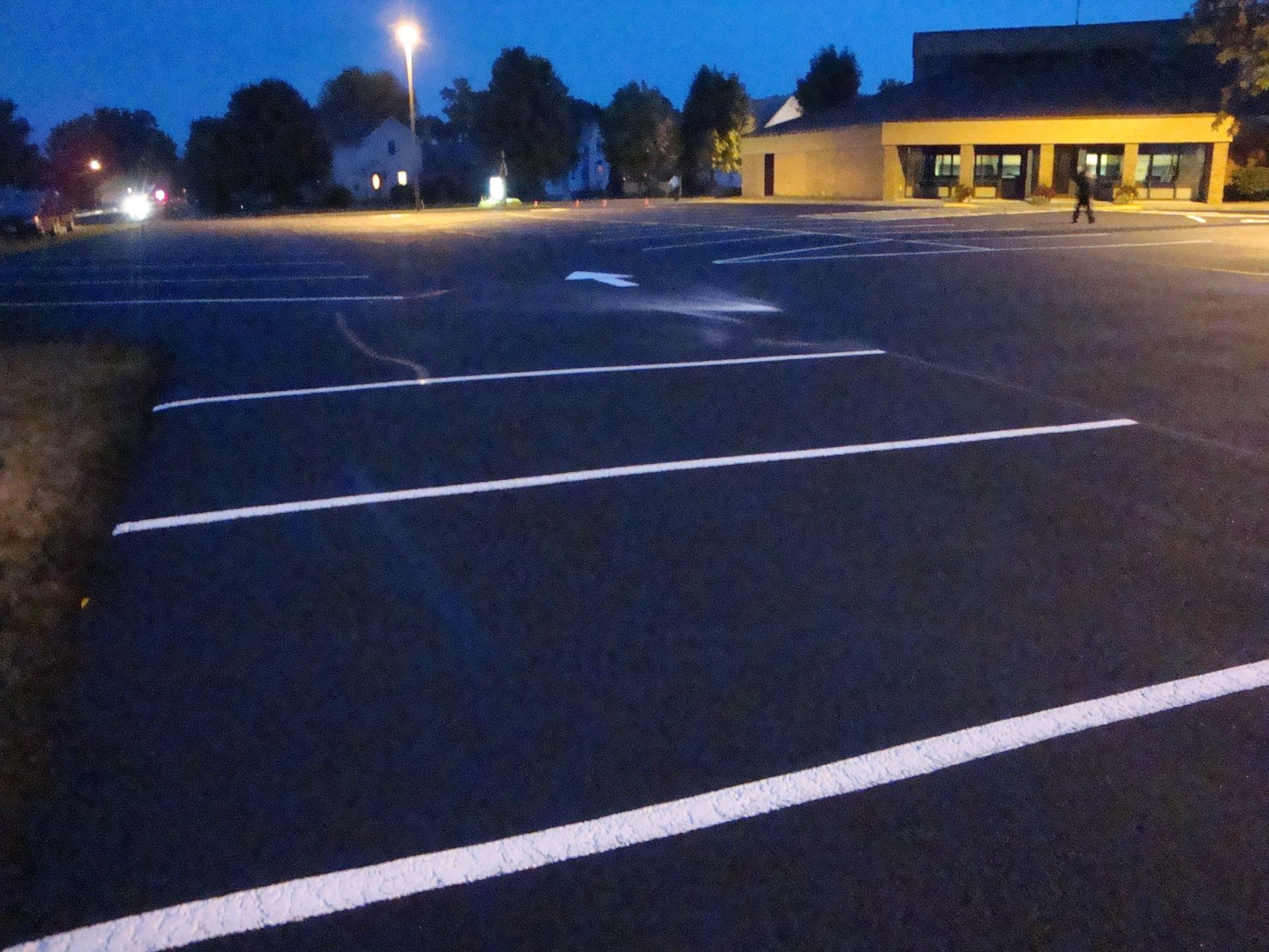 Parking lot at dusk with freshly painted white lines, a building, and a person walking.