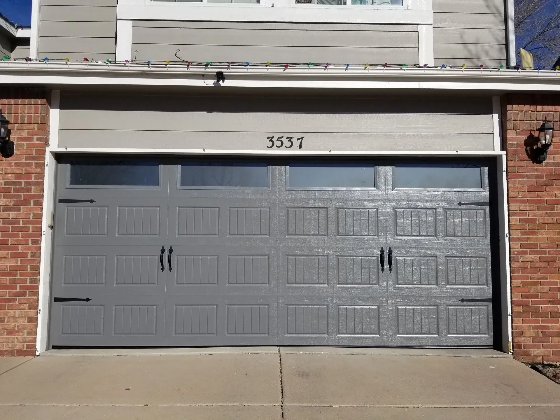Gray garage door with address number 3537 above, set in brick and gray siding.