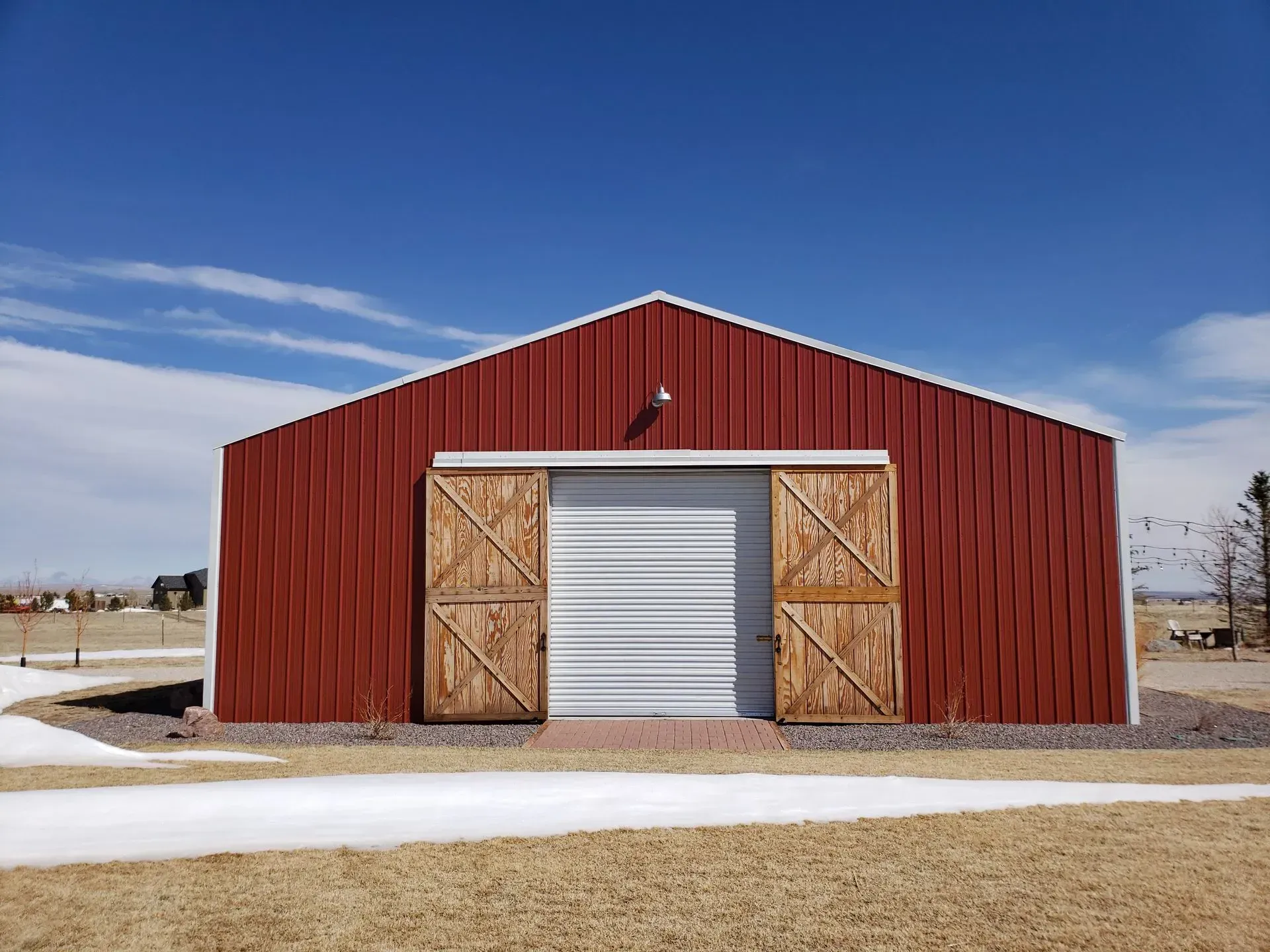 Red barn with wooden sliding doors and white metal garage door, under a blue sky.