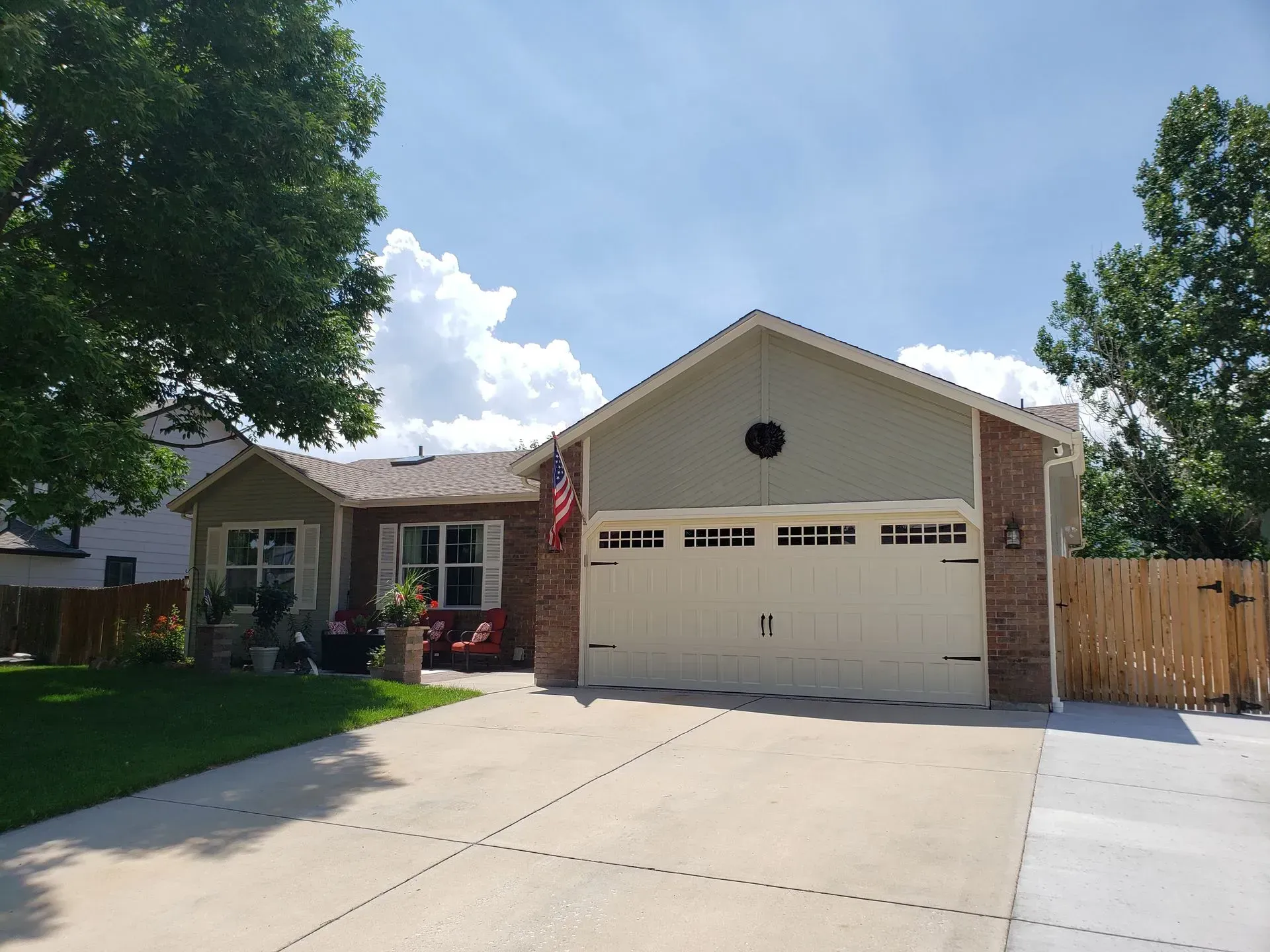 House with beige garage door, red brick facade, and green siding, driveway, and blue sky.