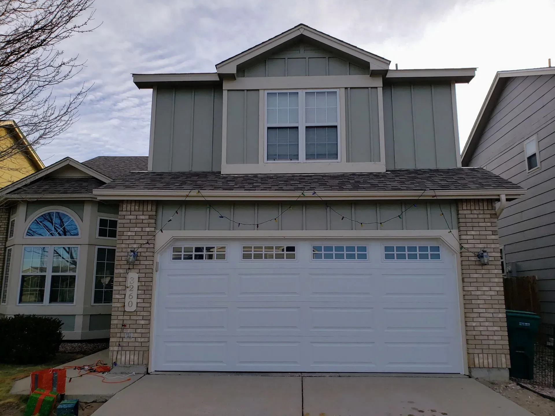 Two-story house with white garage door, light green siding, tan brick, and a cloudy sky.