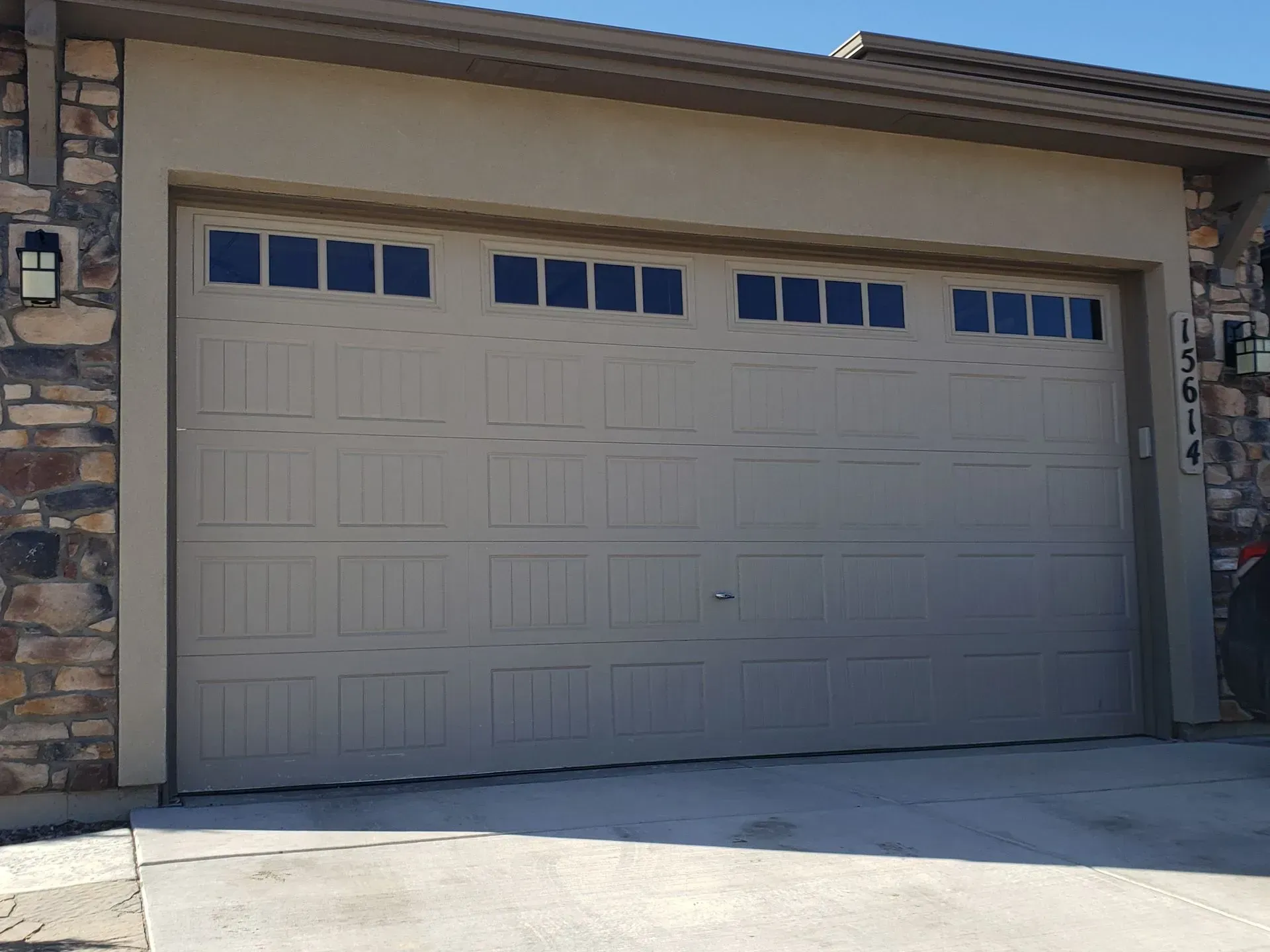 Tan garage door with small windows, set in a light-colored facade with stone accents.