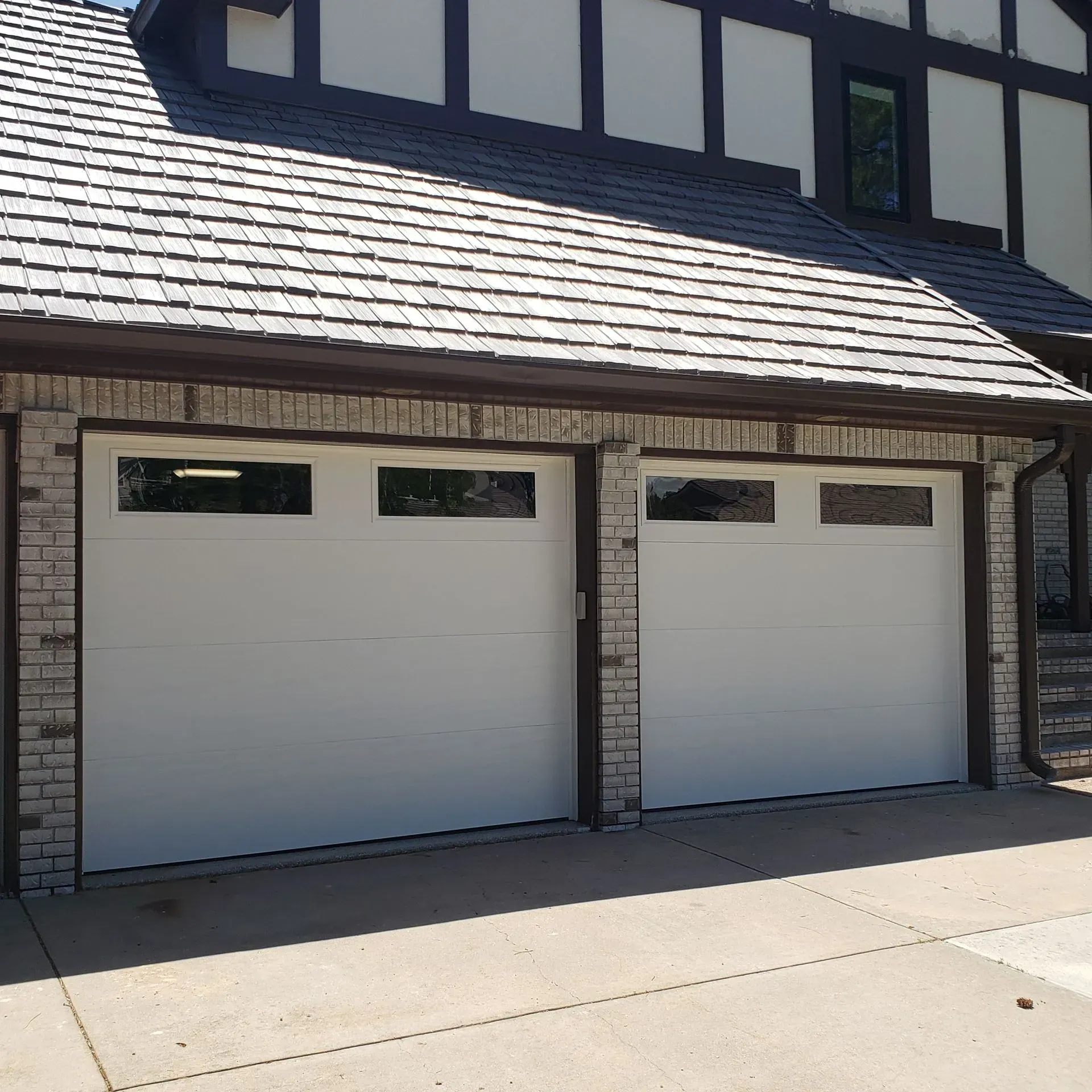 Two white garage doors with windows, brick facade, under a multi-tone roof.