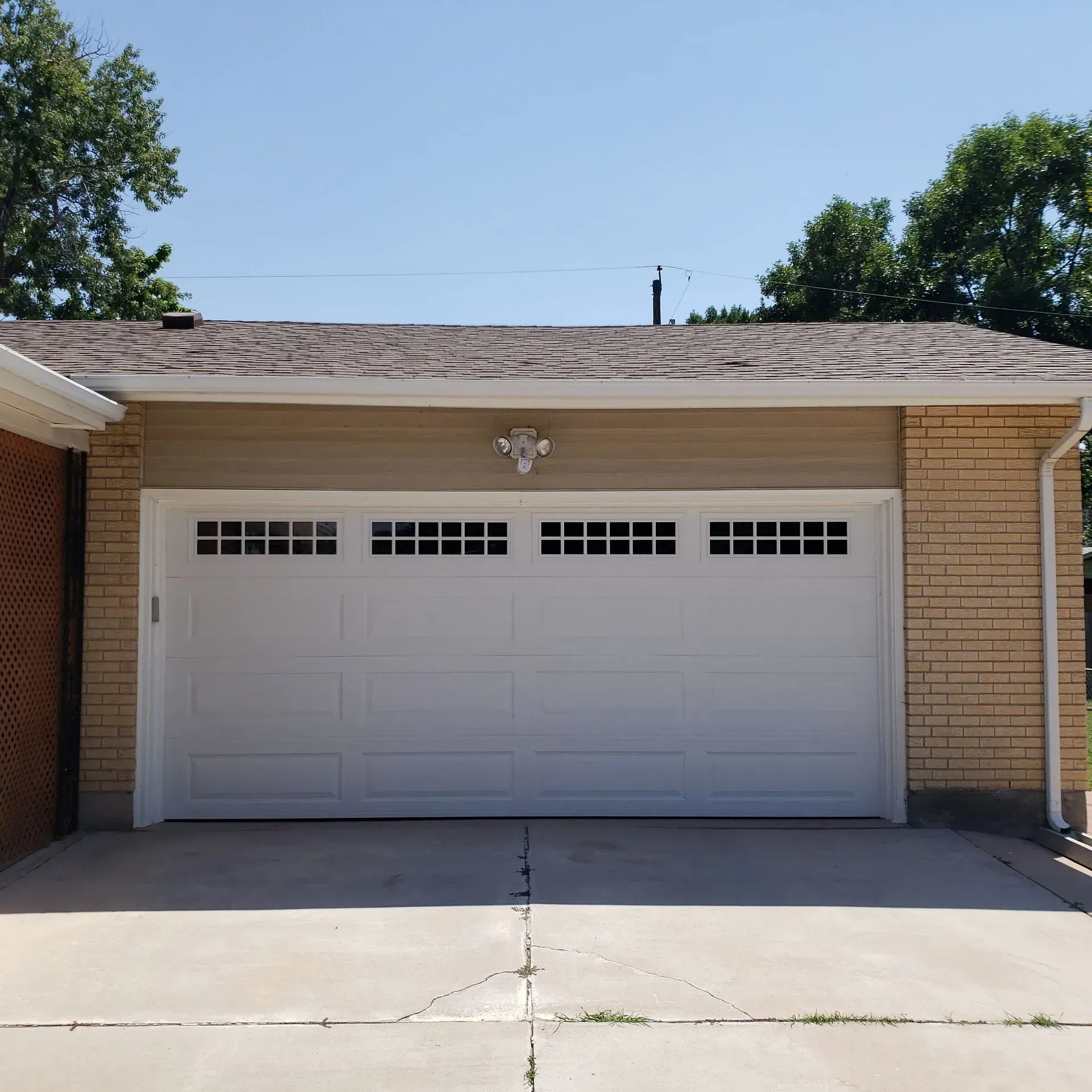 White garage door with windows, on a tan building with a brick wall on one side.