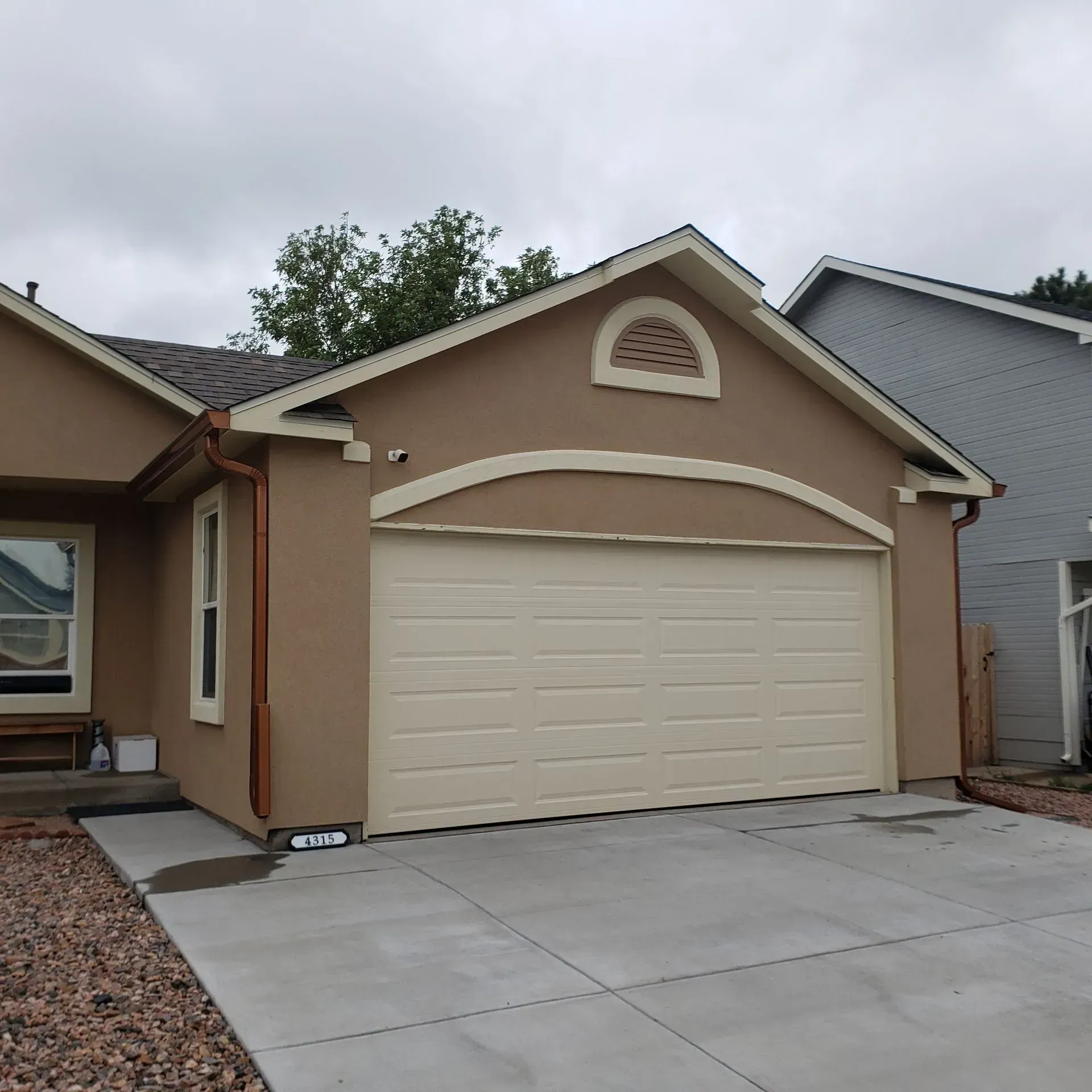 Tan house with a beige garage door and concrete driveway on a cloudy day.