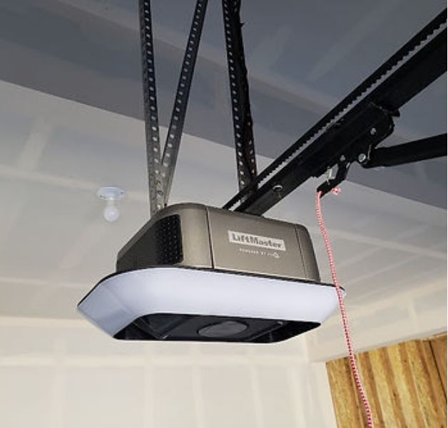 Garage door opener mounted on the ceiling. Brown and silver unit with a white light panel. Red pull cord.