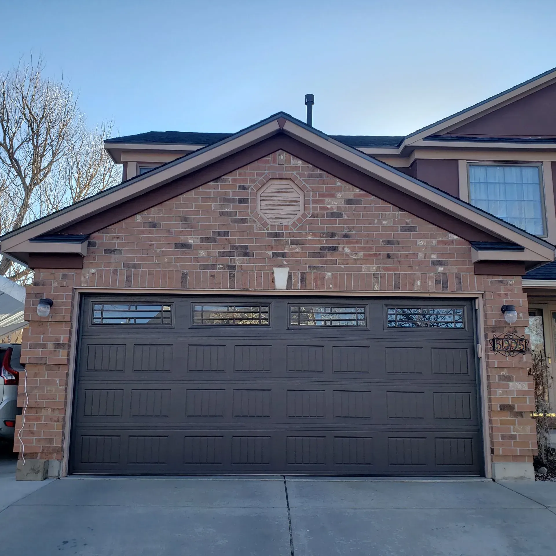 Brown garage door on a brick home with brown trim and windows.