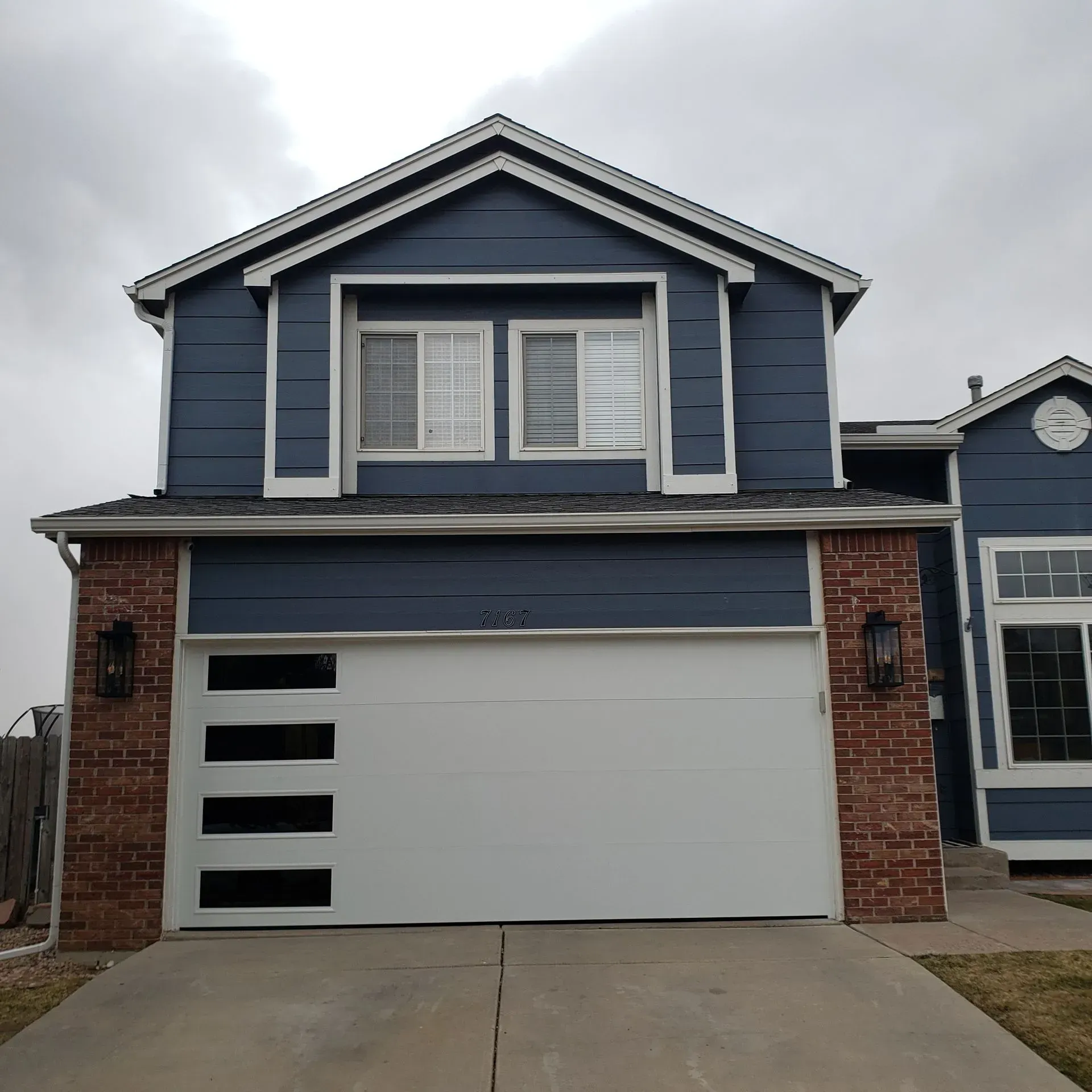 Two-story house with blue siding, white garage door with rectangular windows, and a brick facade.