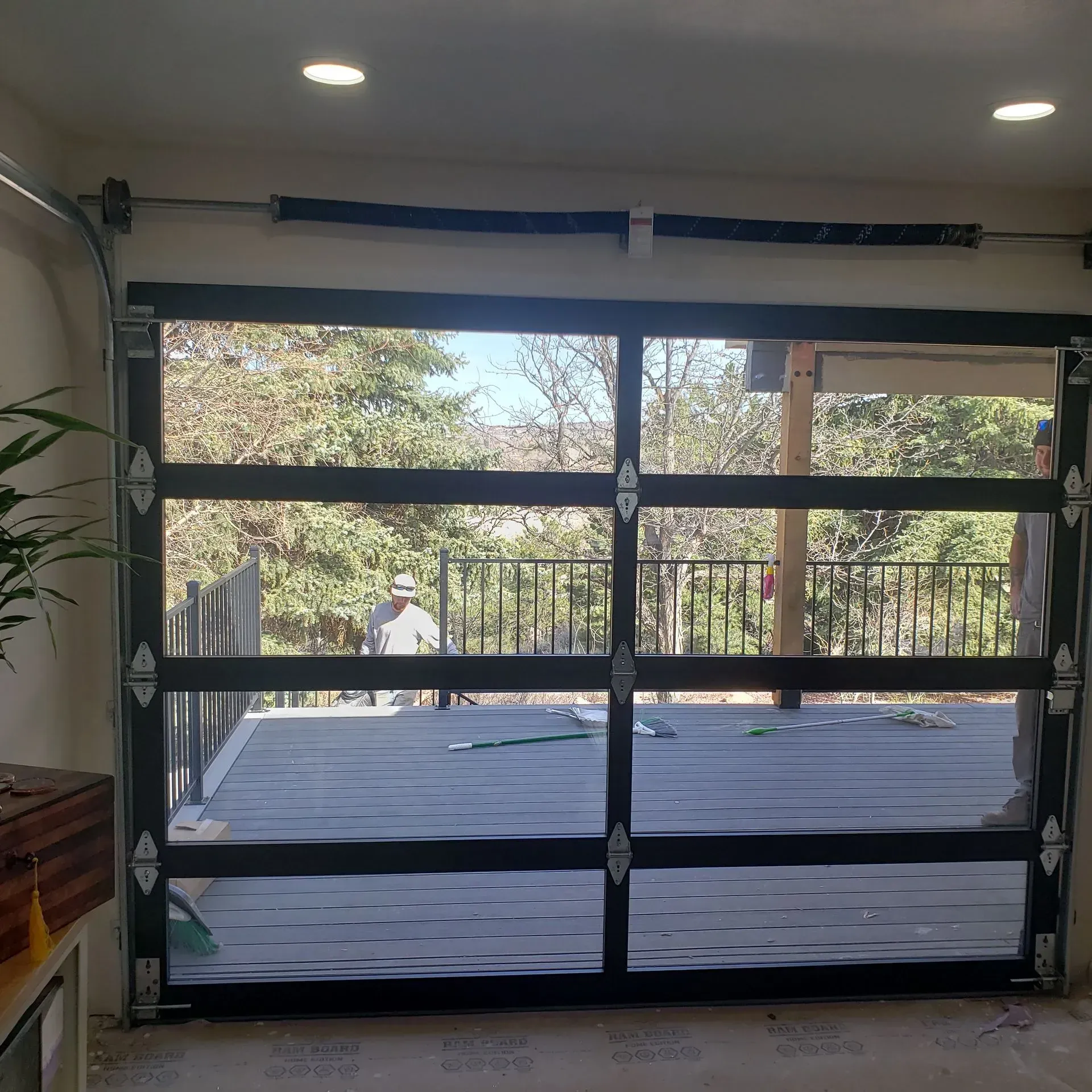 Glass garage door, open to a deck with a person visible. Black frame, sunny day.