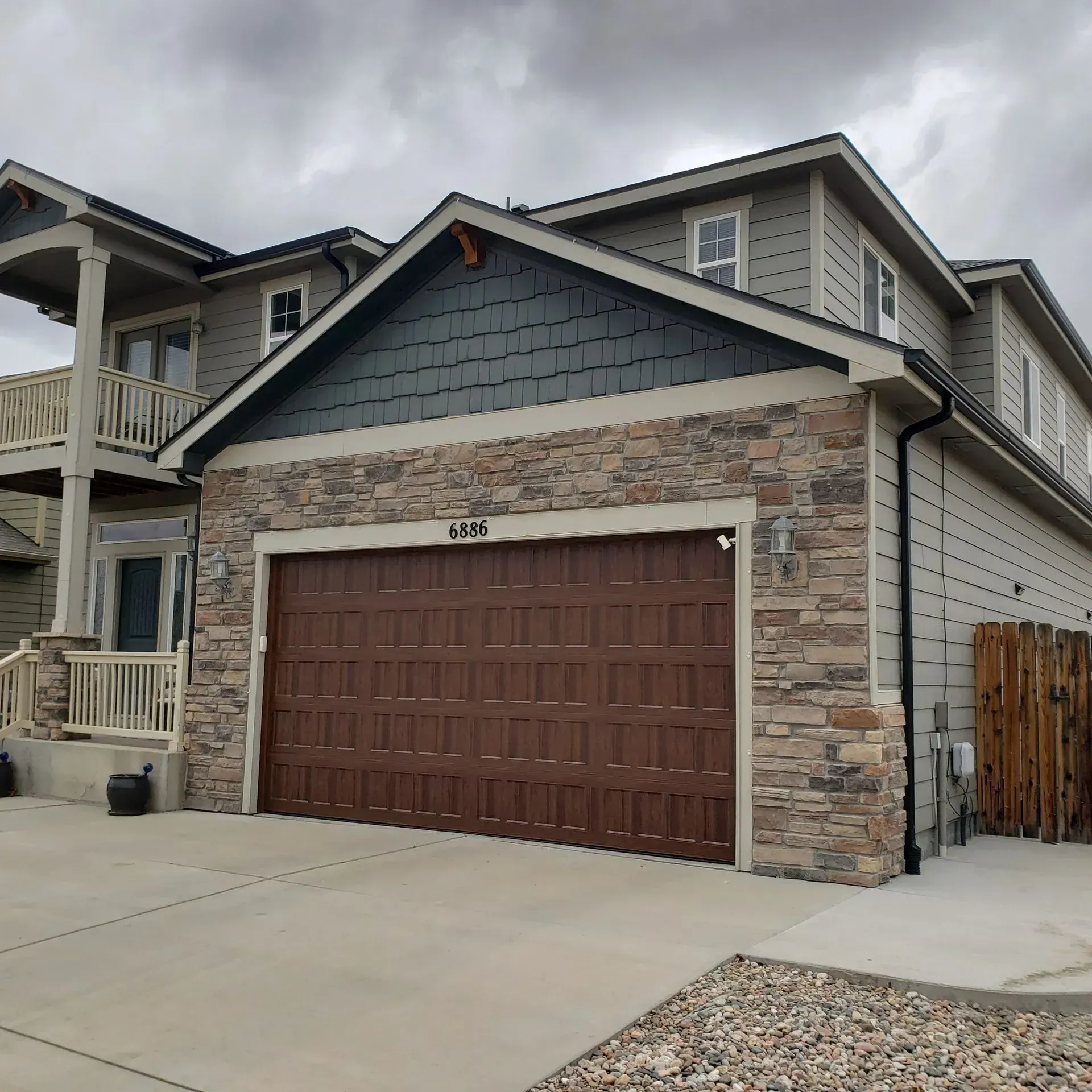 House with brown garage door, stone facade, gray siding, and a cloudy sky.
