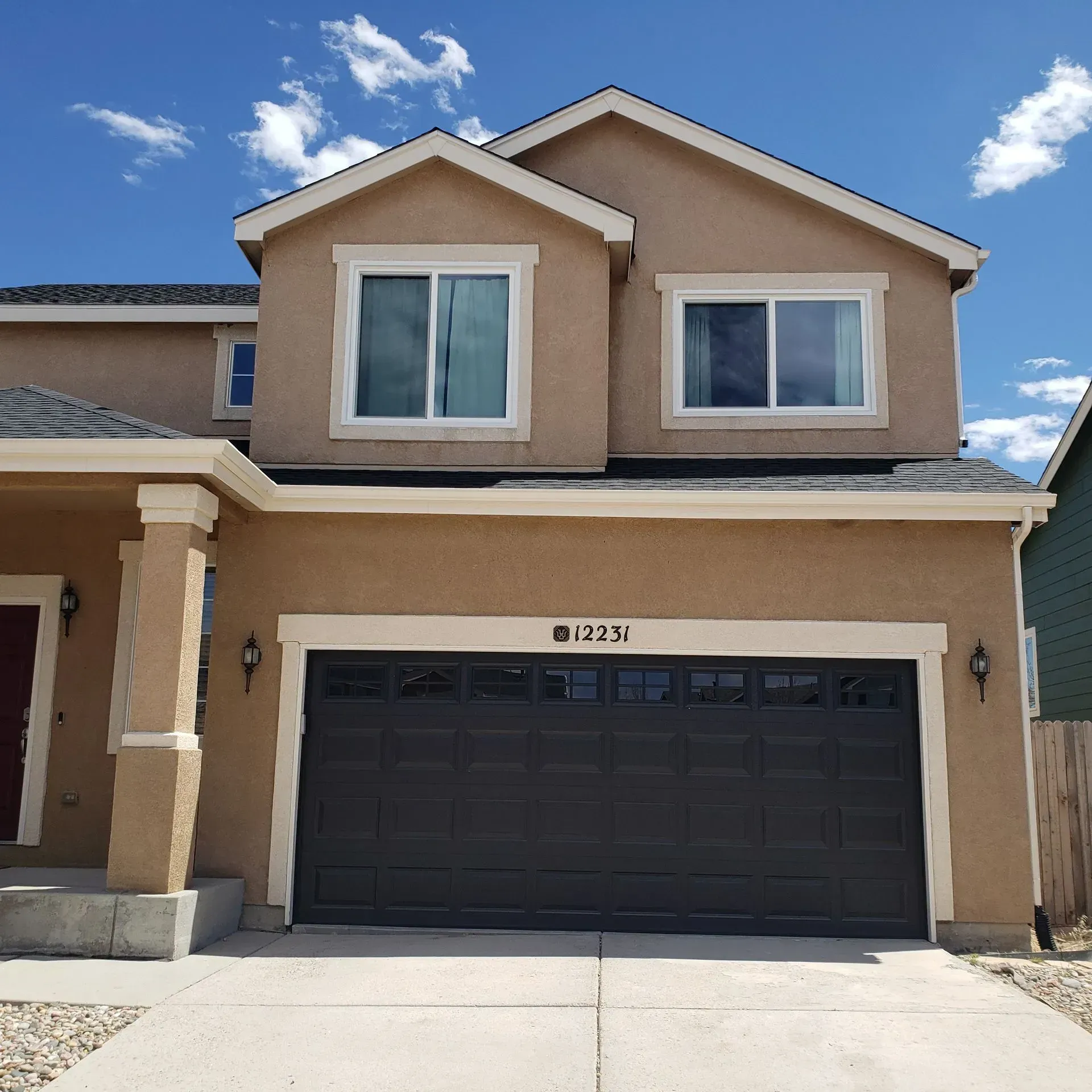 Tan two-story house with a black garage door and blue sky.