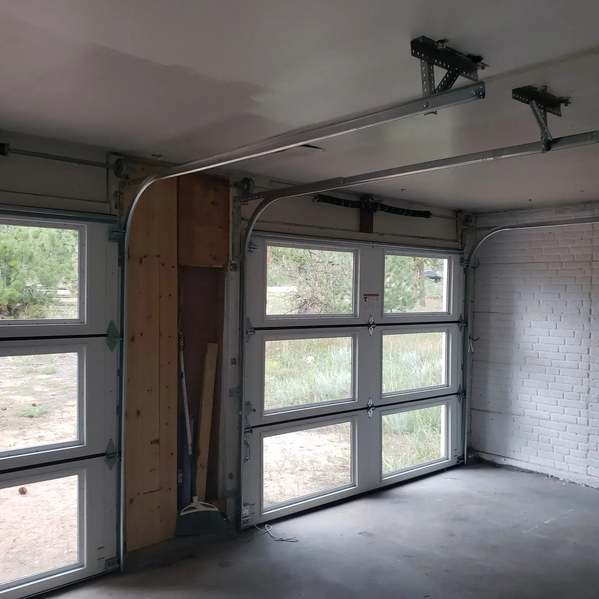 Interior view of a garage with glass-paned doors. One door is open, showing a wooded outdoor view.