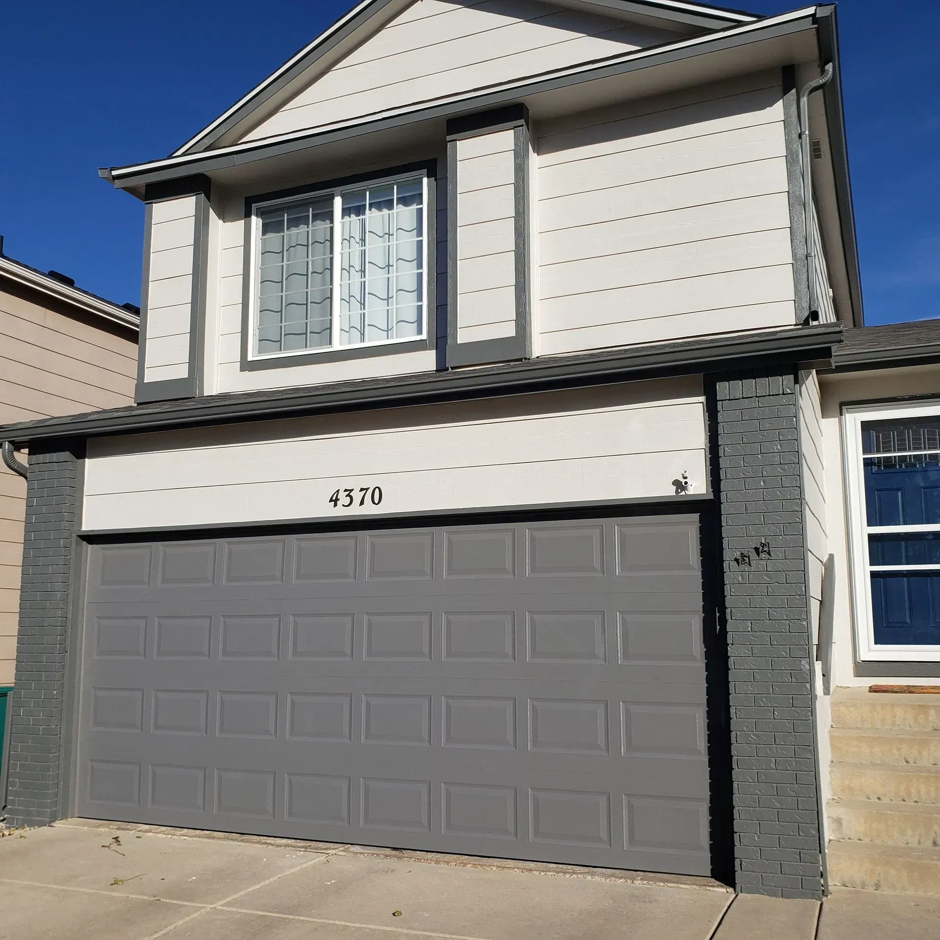 Two-story house with gray garage door, white siding, and a window. Address number 370 is above the garage.