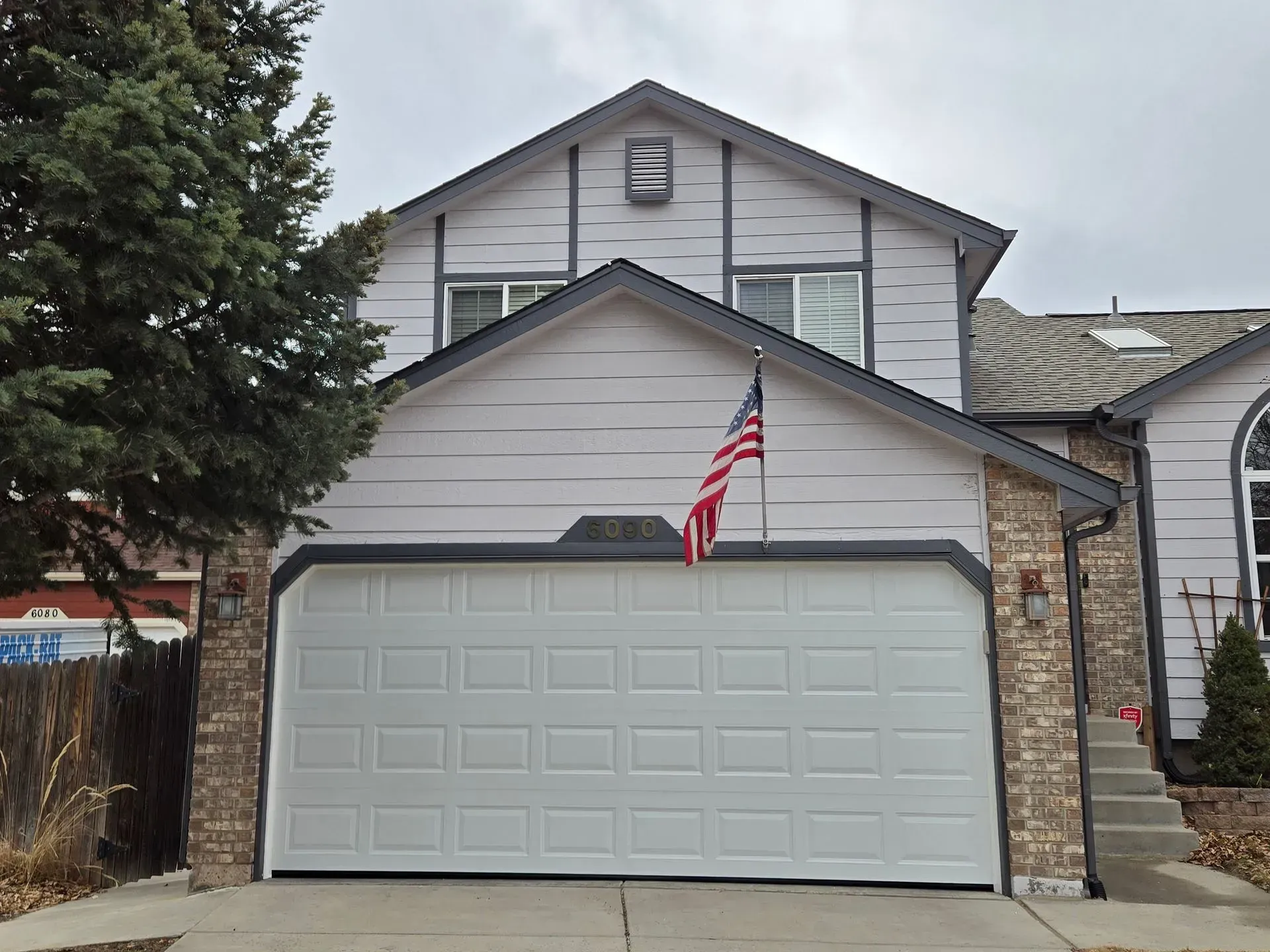 Two-story house with white garage door, American flag, and gray siding.