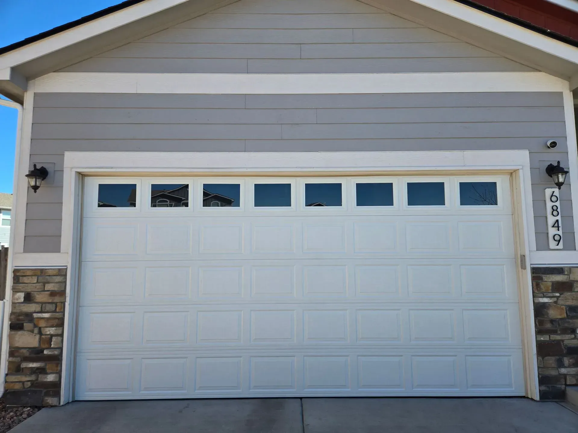 White garage door with windows, on a house with gray siding and stone accents.