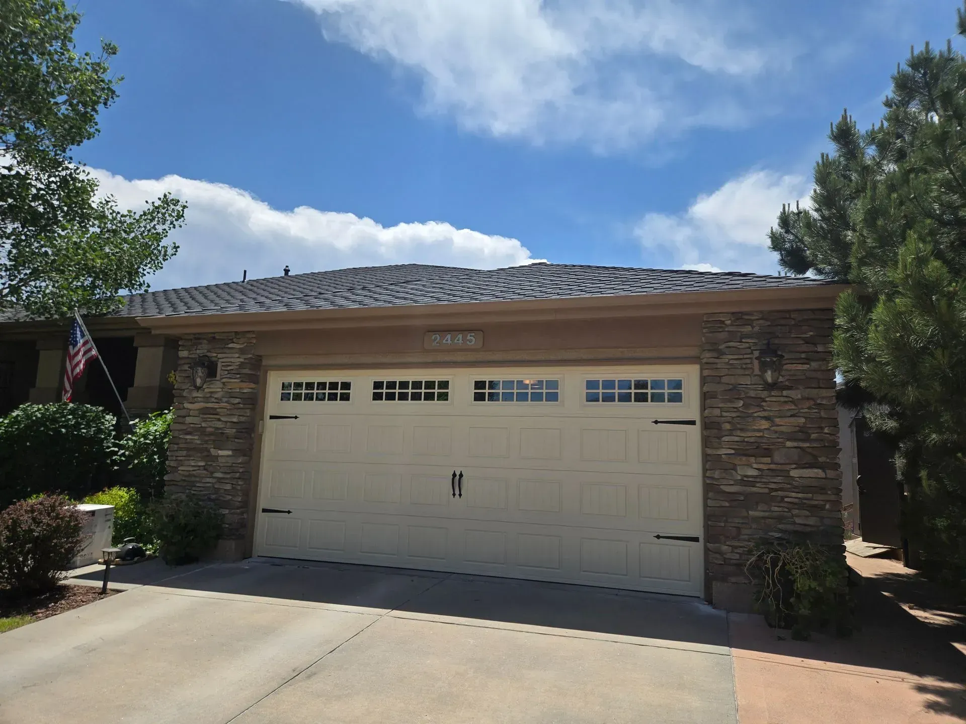 Garage with tan door, stone accents, and dark roof under a blue sky.