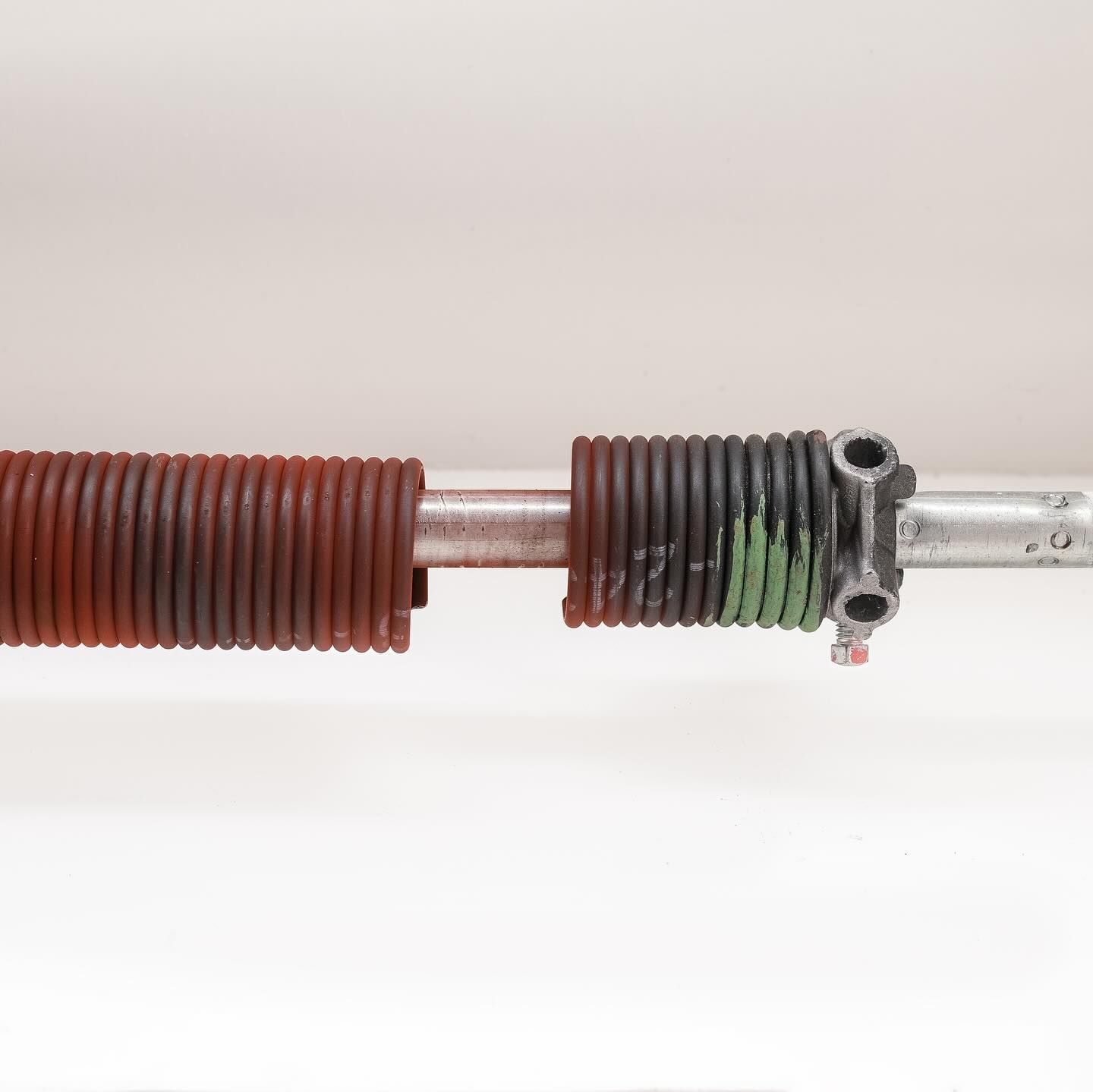 Garage door torsion spring, rusty red and black, mounted on a silver rod.