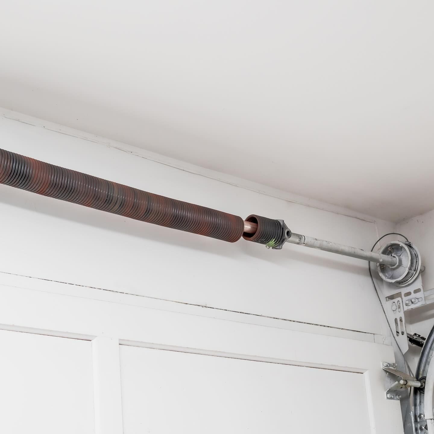 Garage door torsion spring, brown and rusty, above a white garage door.