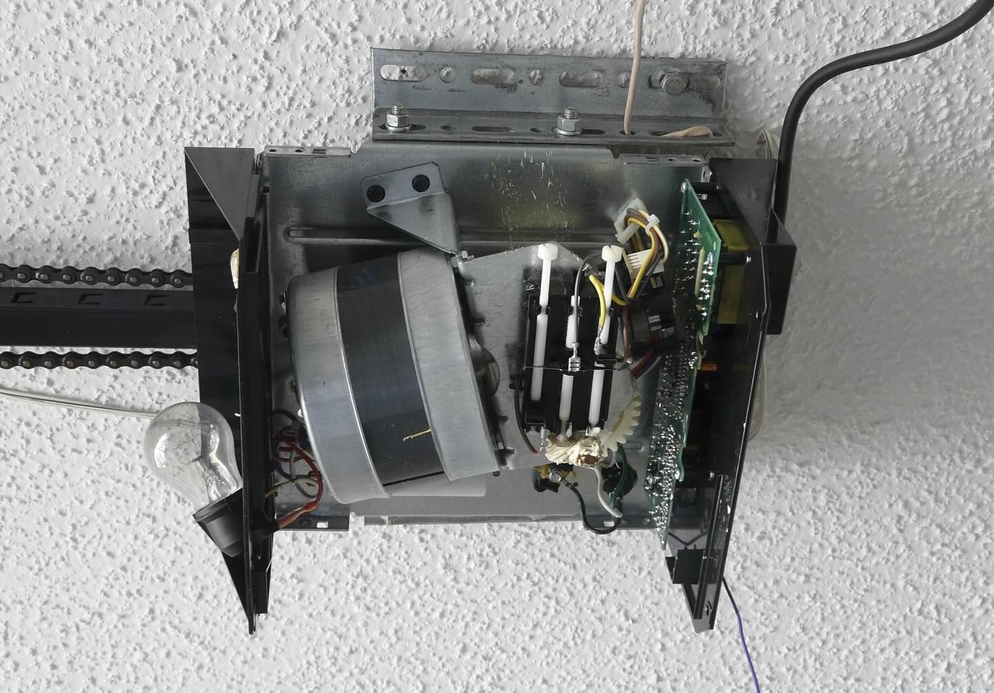Garage door opener motor, chain drive, mounted on white ceiling. Metal, black, and silver components visible.