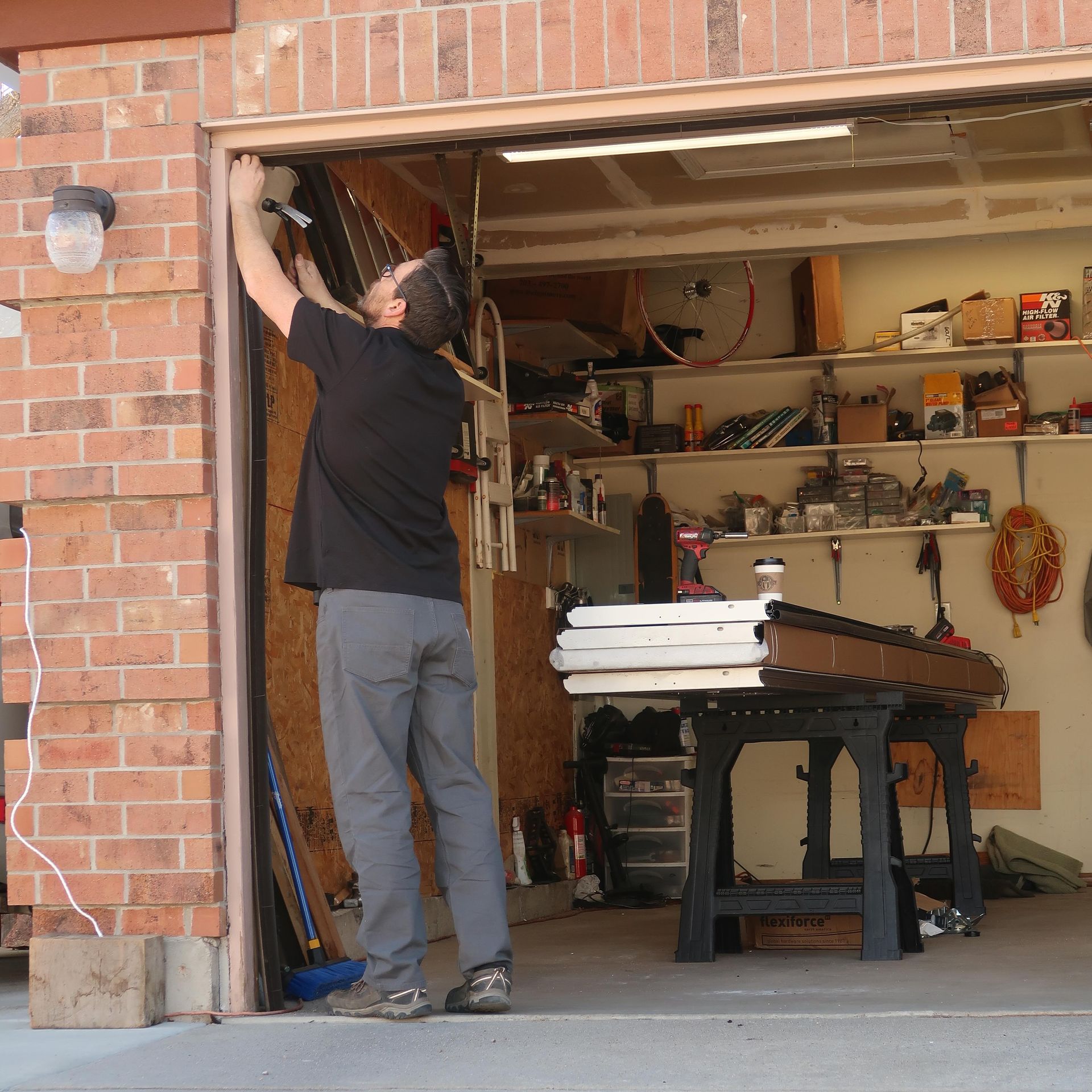 Man installs garage door trim, working inside the open garage, with tools and supplies nearby.
