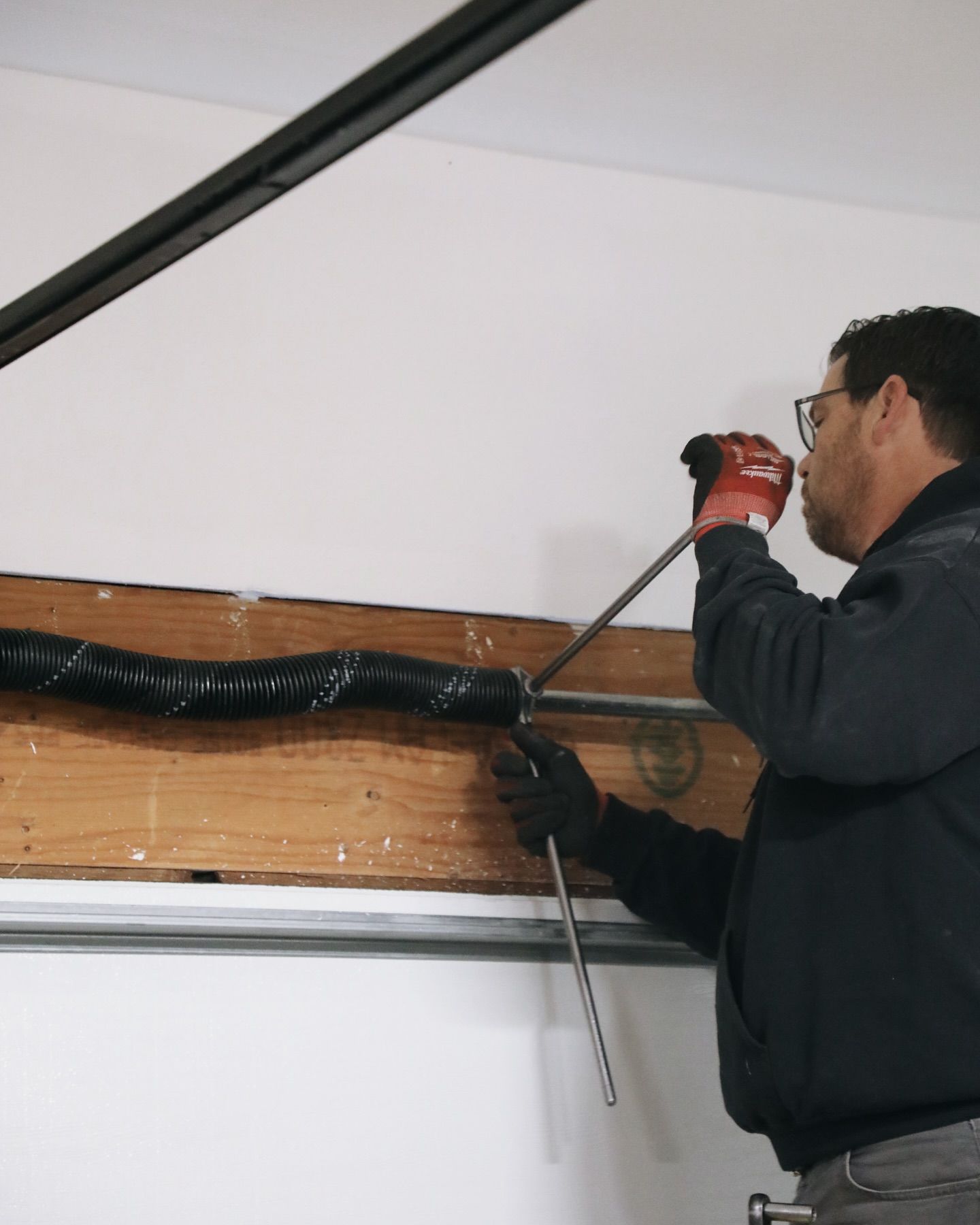Man in gloves working on garage door spring with tools.