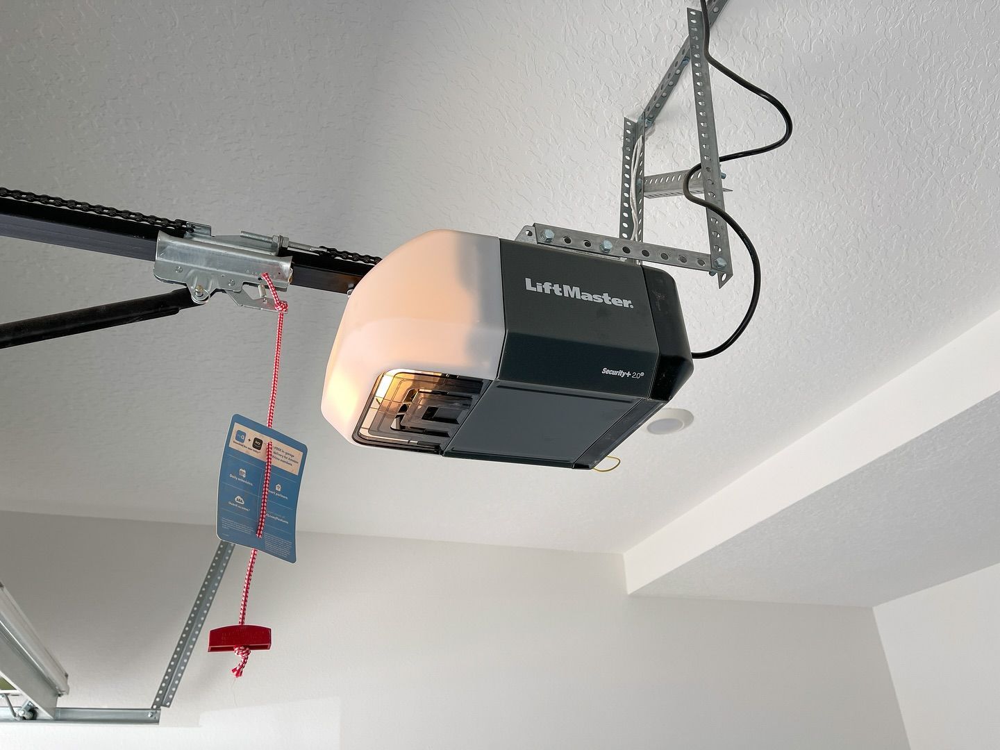 Garage door opener attached to the ceiling, with red emergency cord hanging.