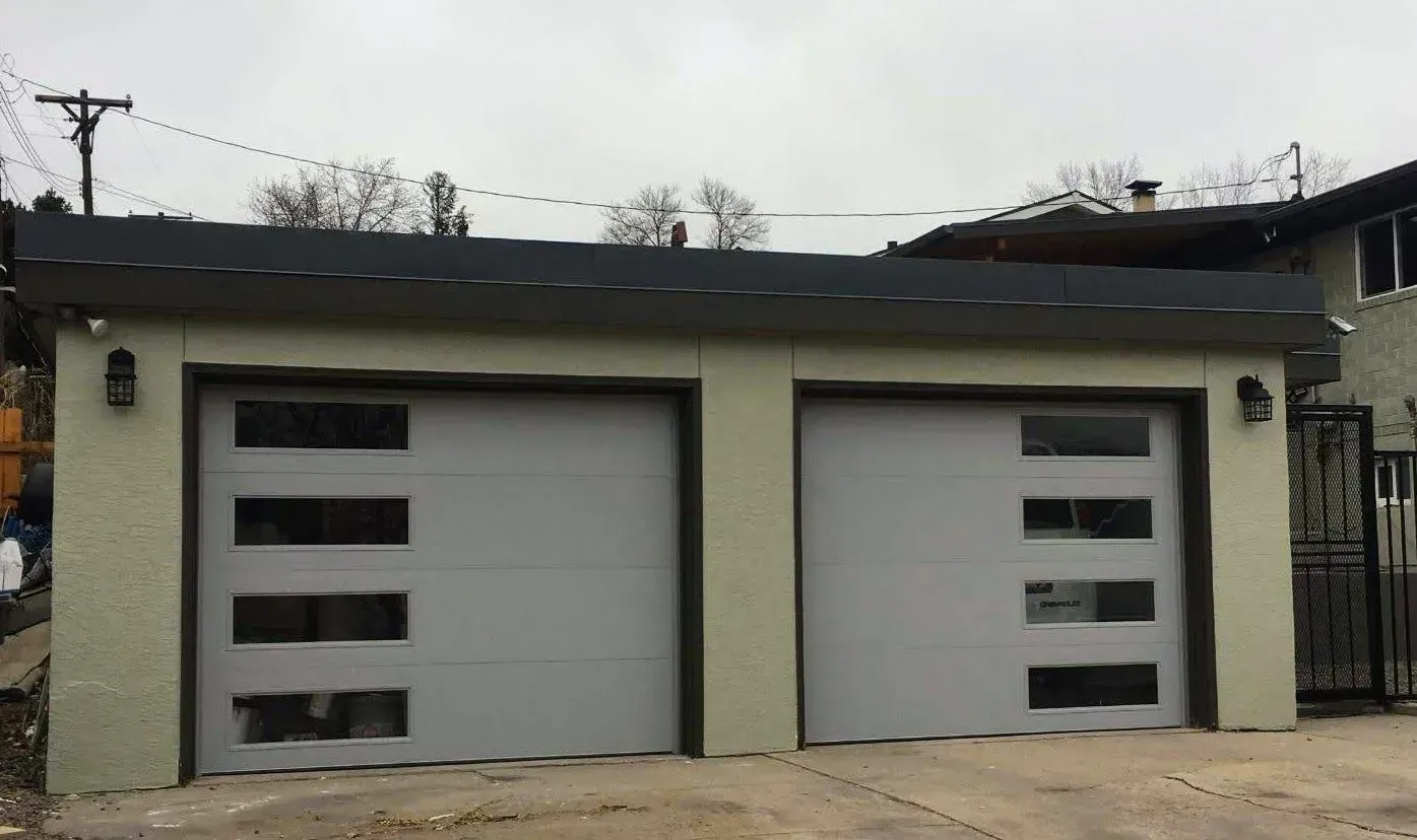 Two-car garage with light gray doors and rectangular windows. Building is light green with a dark gray roof.