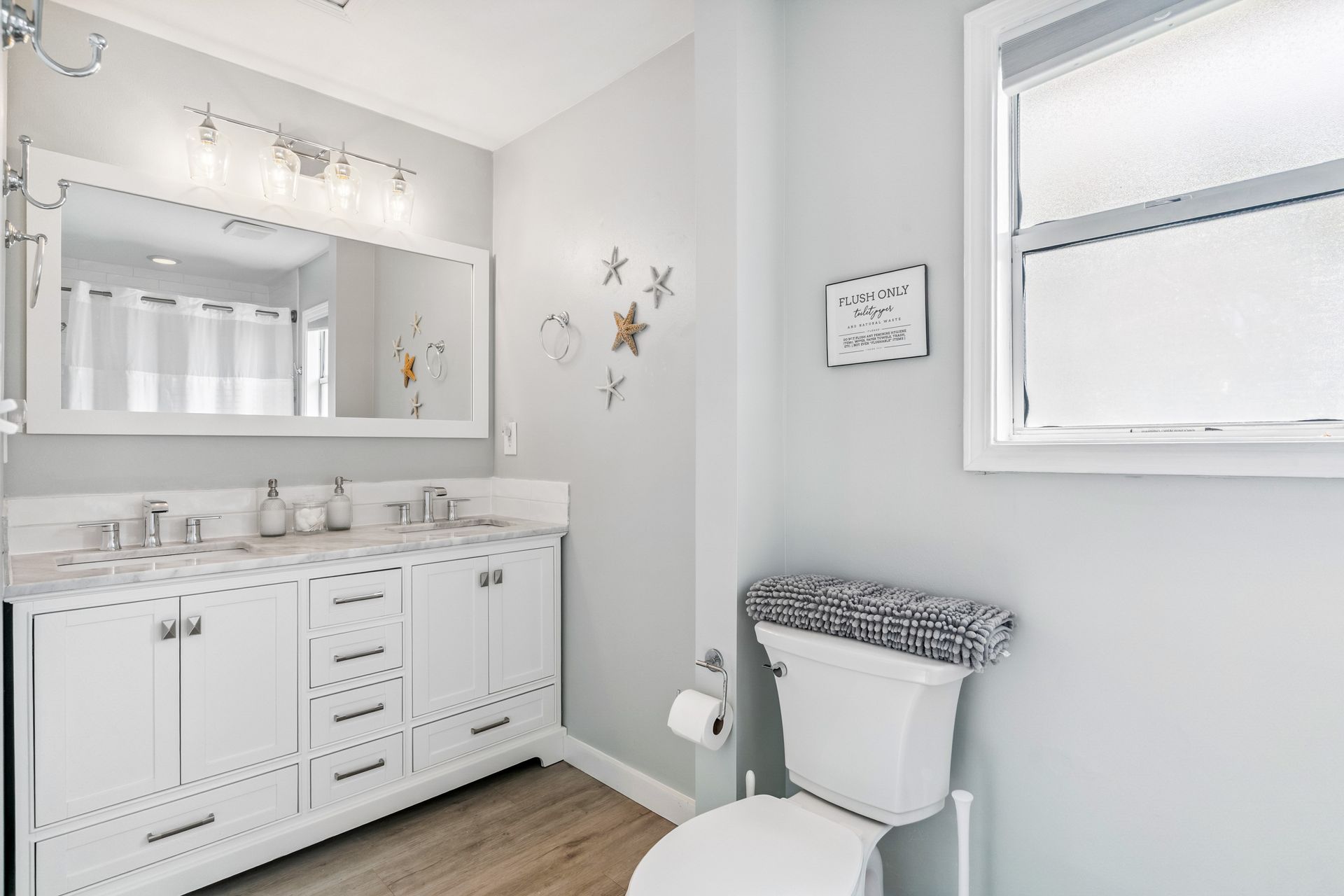 A bathroom with a toilet , sink , mirror and window.