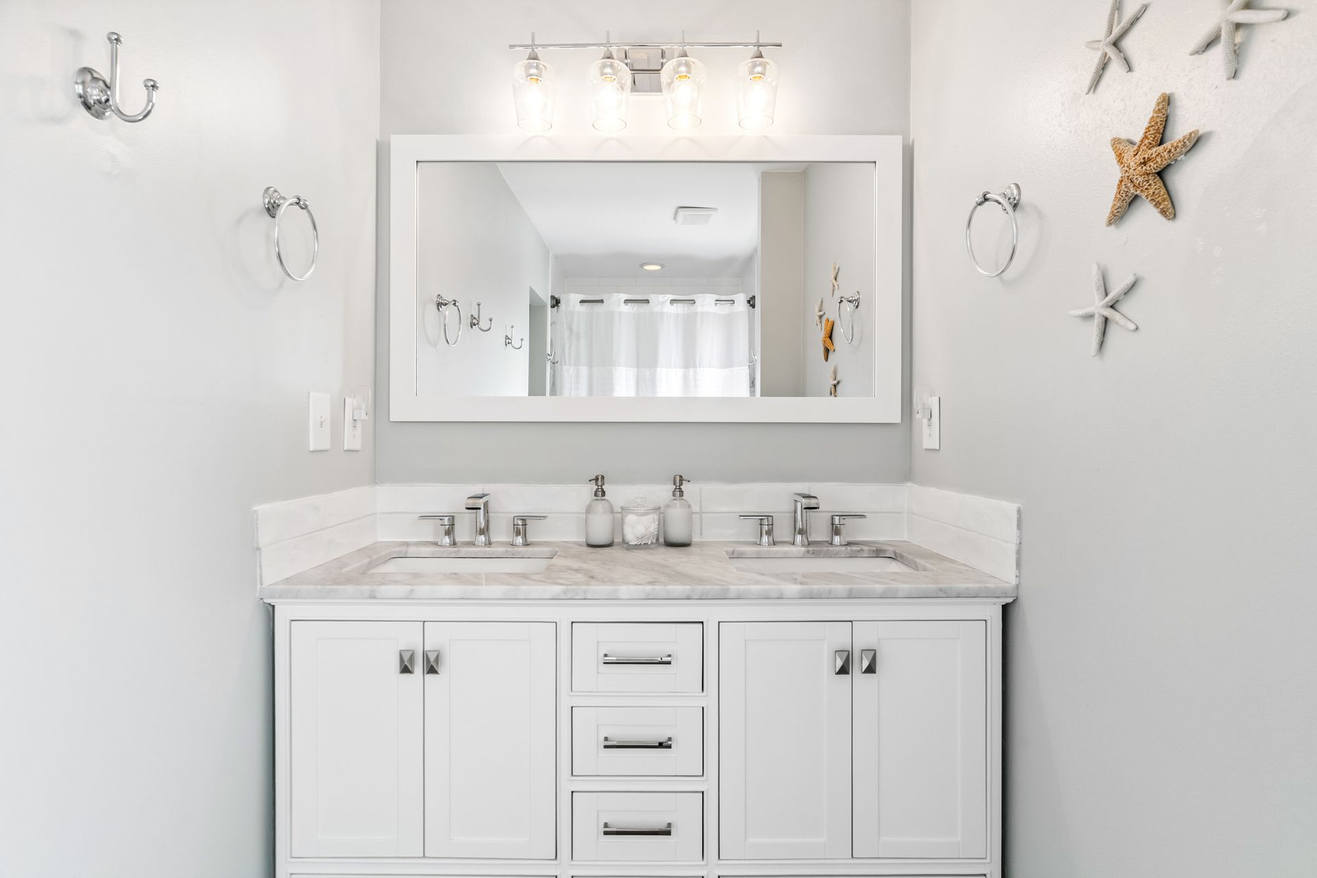 A bathroom with two sinks , a mirror and starfish on the wall.