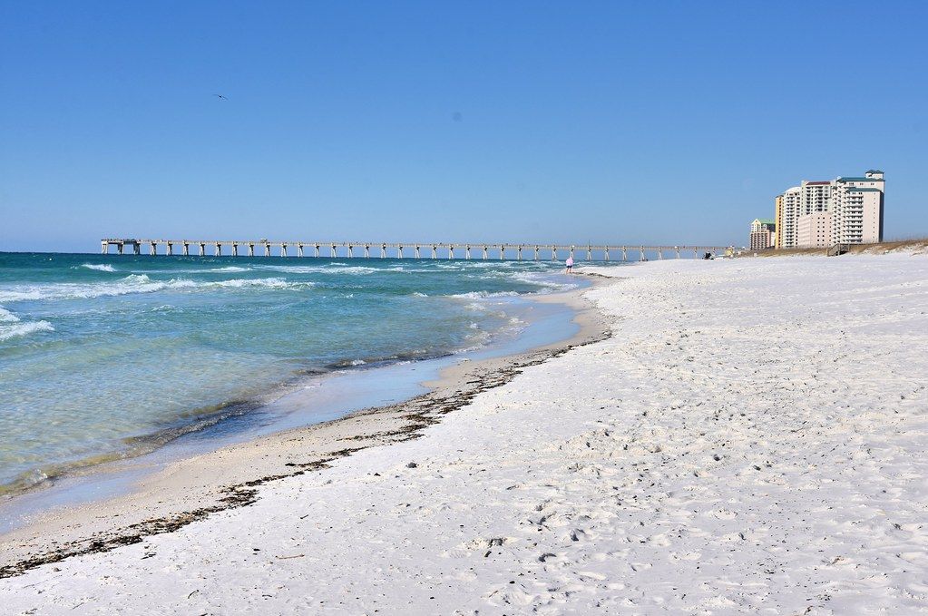 A beach with white sand and a pier in the background
