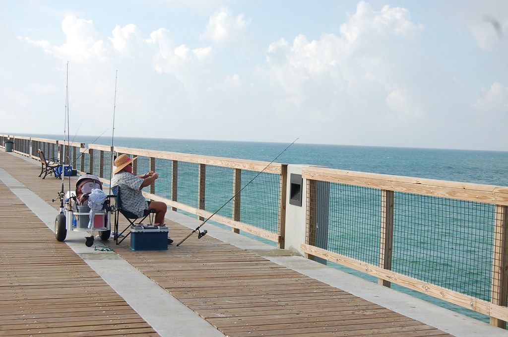 A man is fishing on a pier next to the ocean