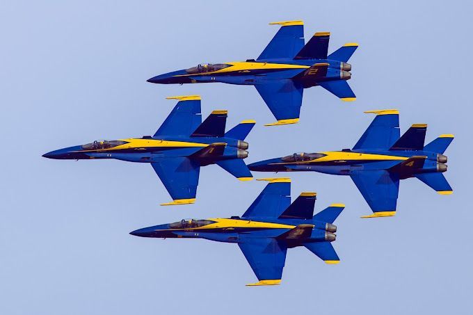 Four blue and yellow fighter jets are flying in formation