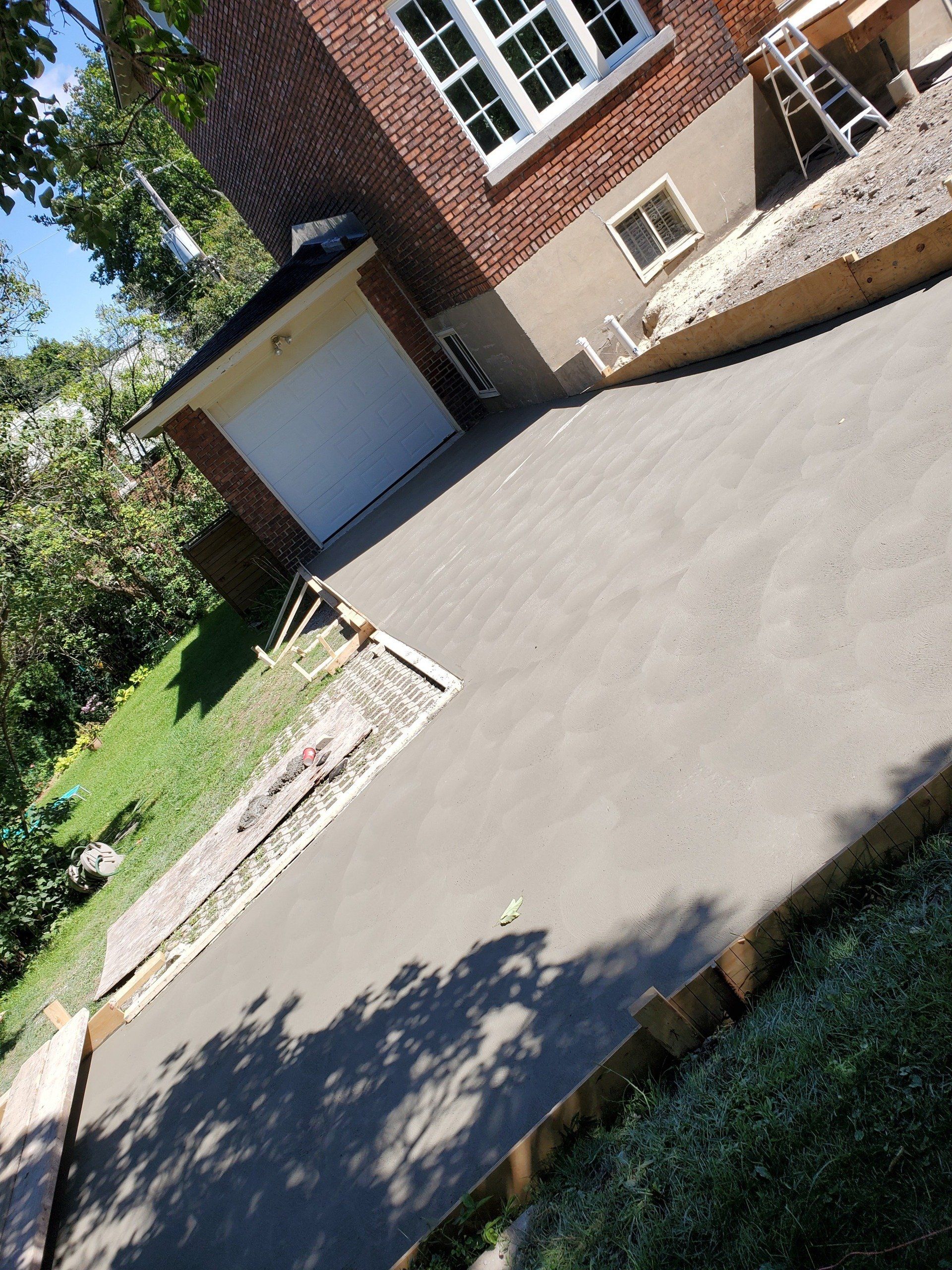 A concrete driveway is being built in front of a brick house.