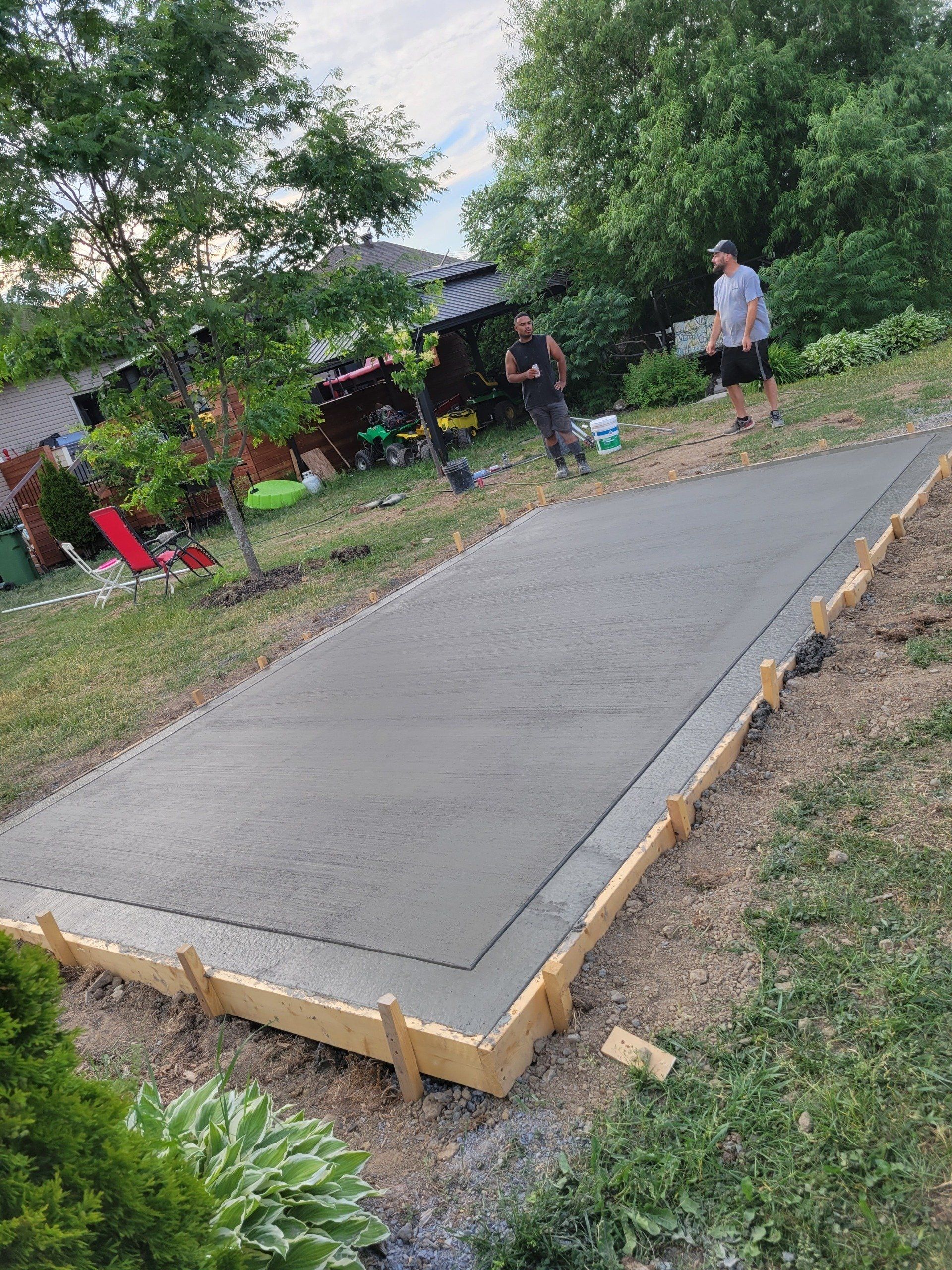 Two men are standing on top of a concrete slab in a backyard.