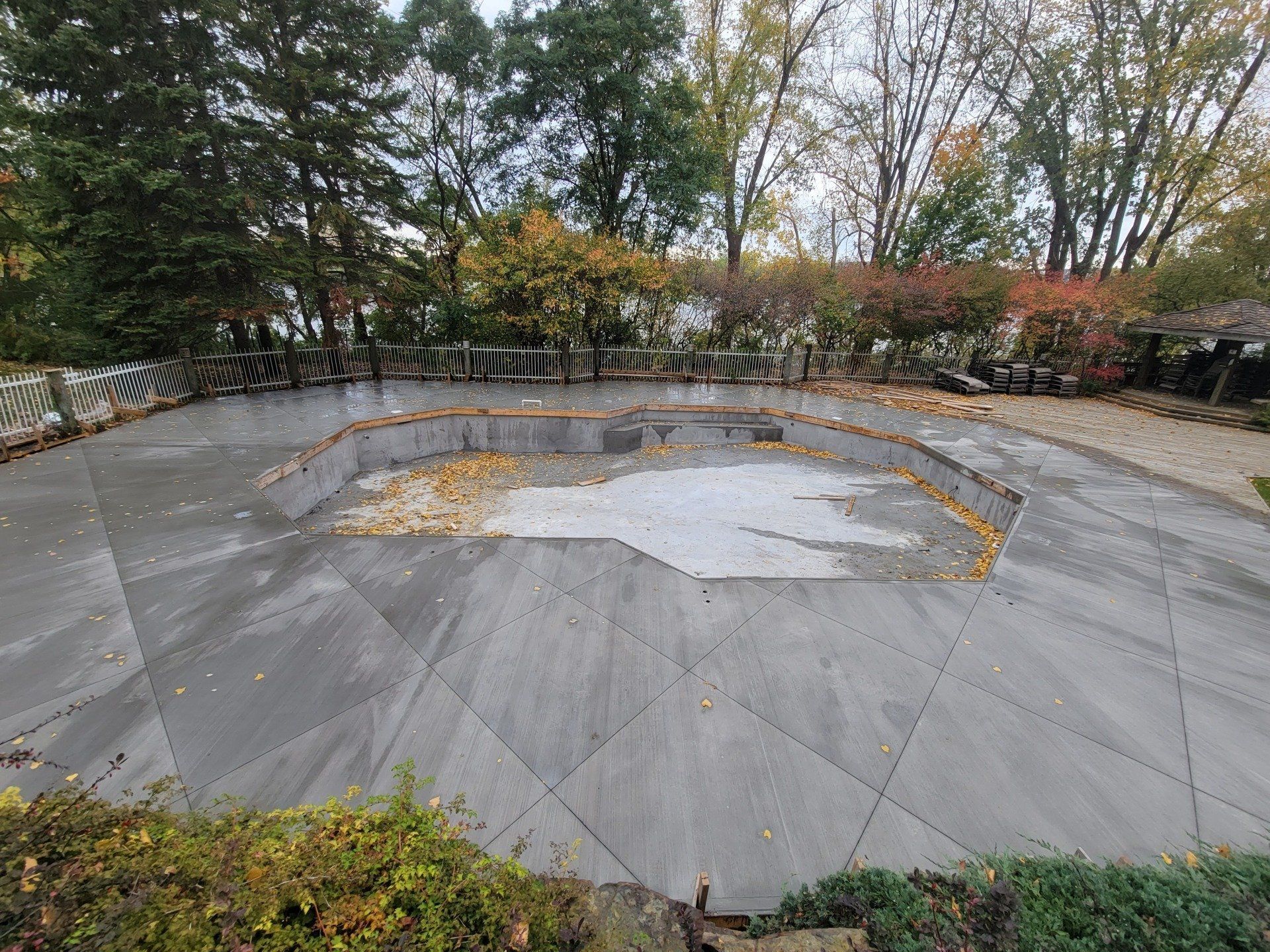 A large concrete patio with a swimming pool in the middle of it surrounded by trees.