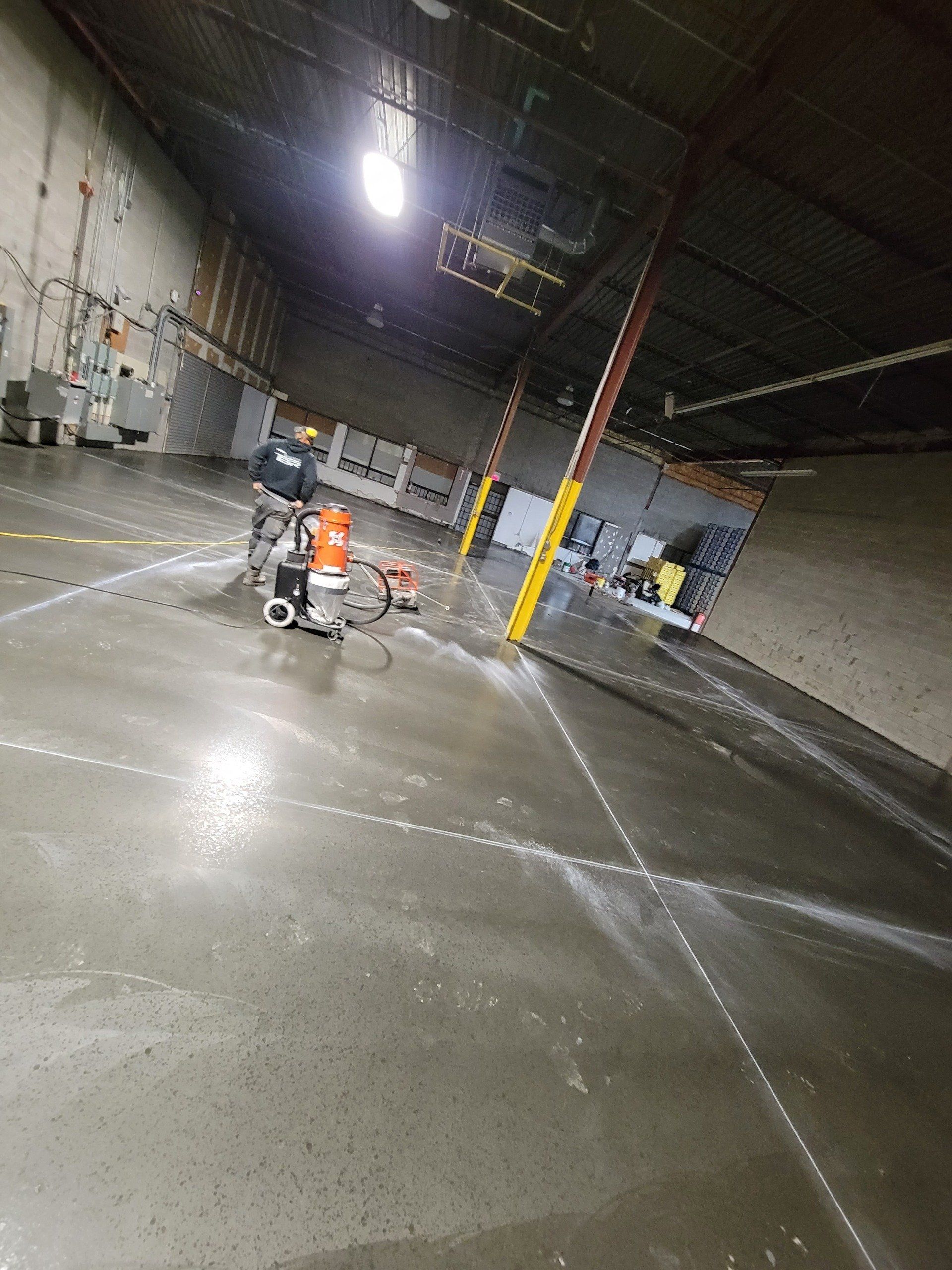 A man is cleaning a concrete floor in a large warehouse.
