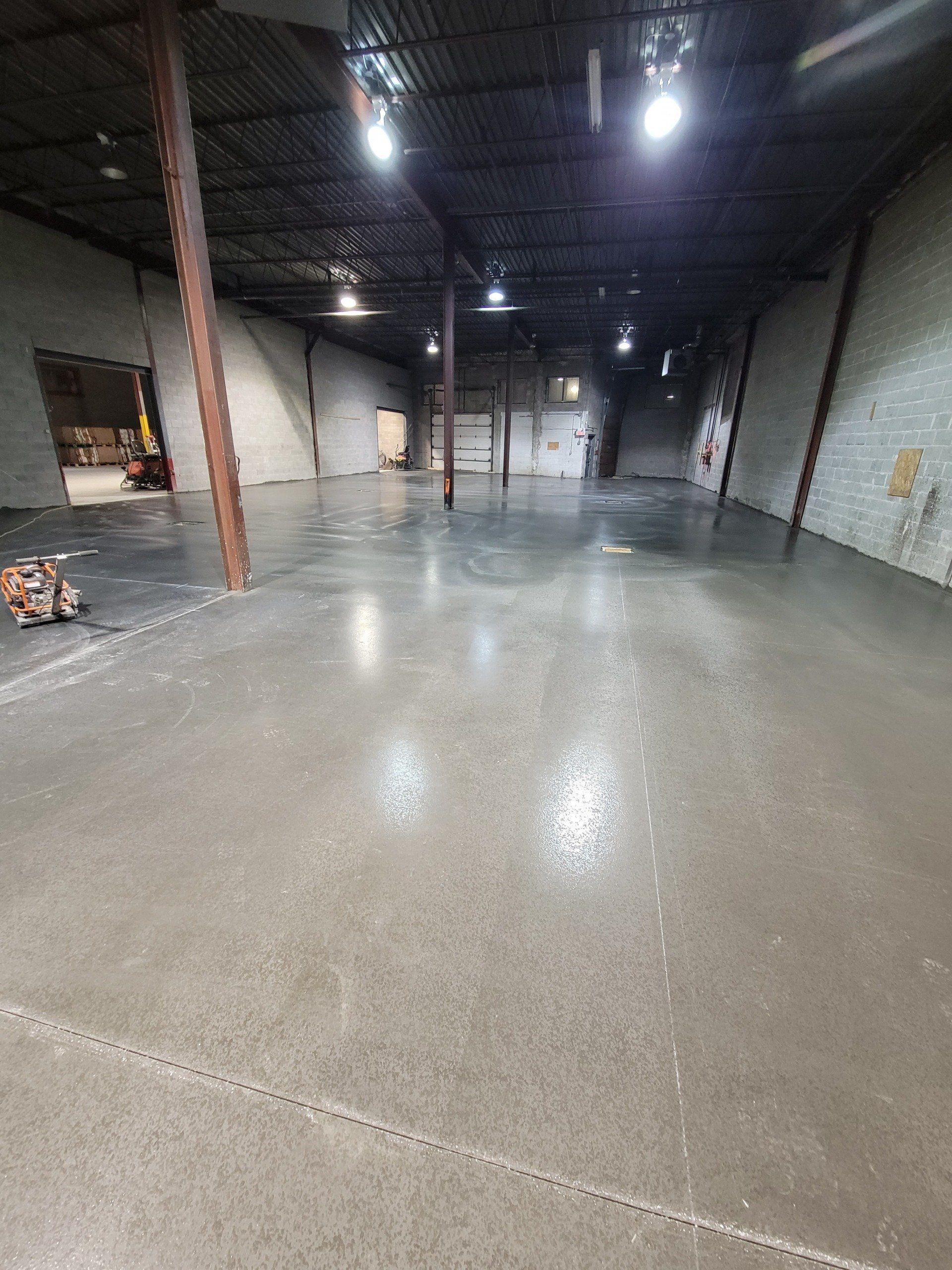 Intérieur d'entrepôt vide et spacieux avec sol en béton poli, plafonniers et poutres de support.