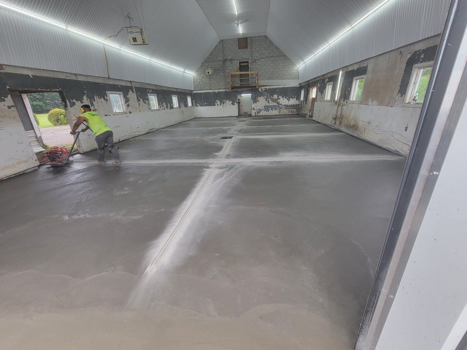 Un homme utilise une meuleuse à béton dans une grange avec un sol en béton gris.