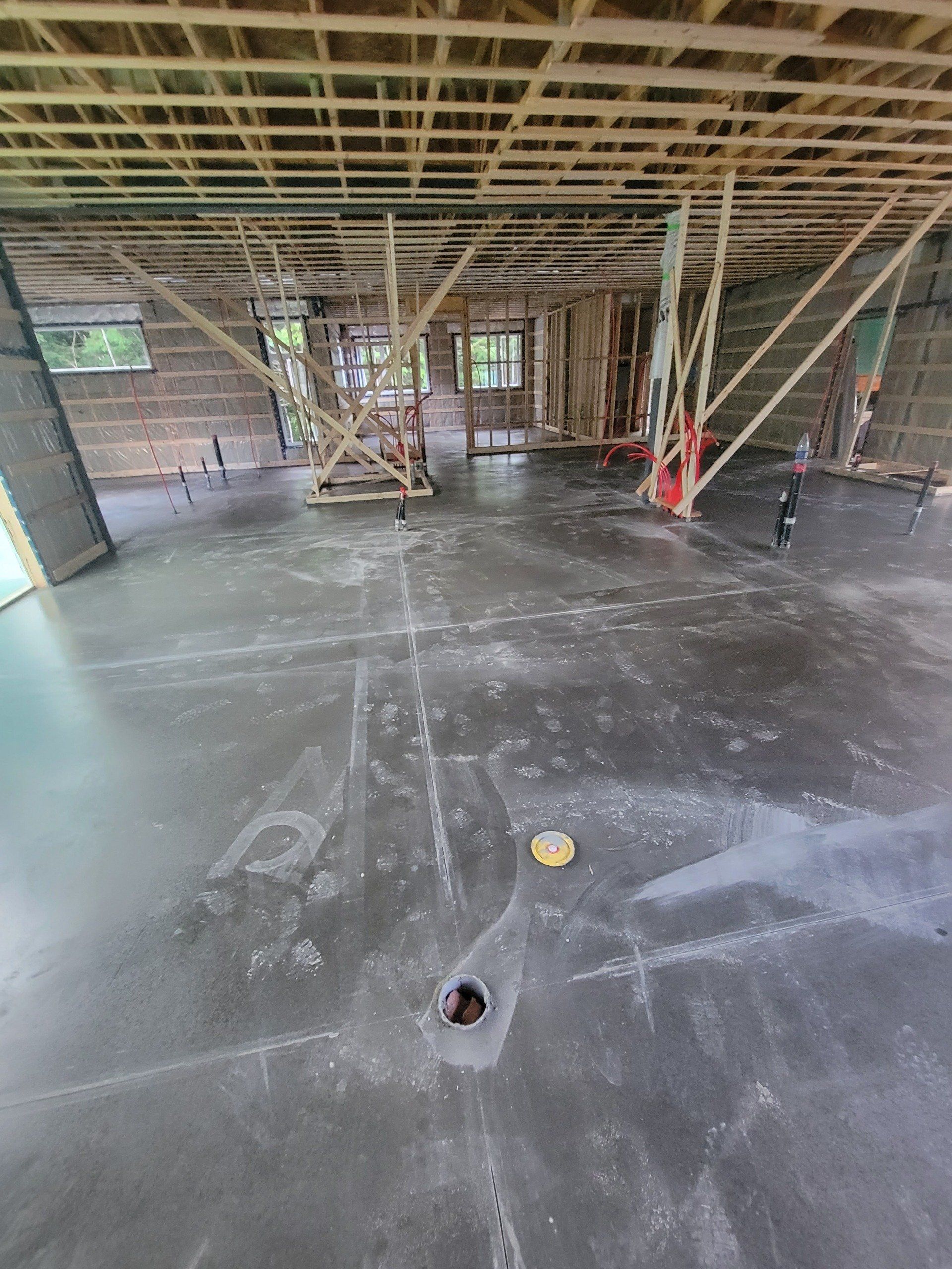 Vue intérieure d'un bâtiment en construction : poutres en bois apparentes, plancher en béton et structures porteuses.