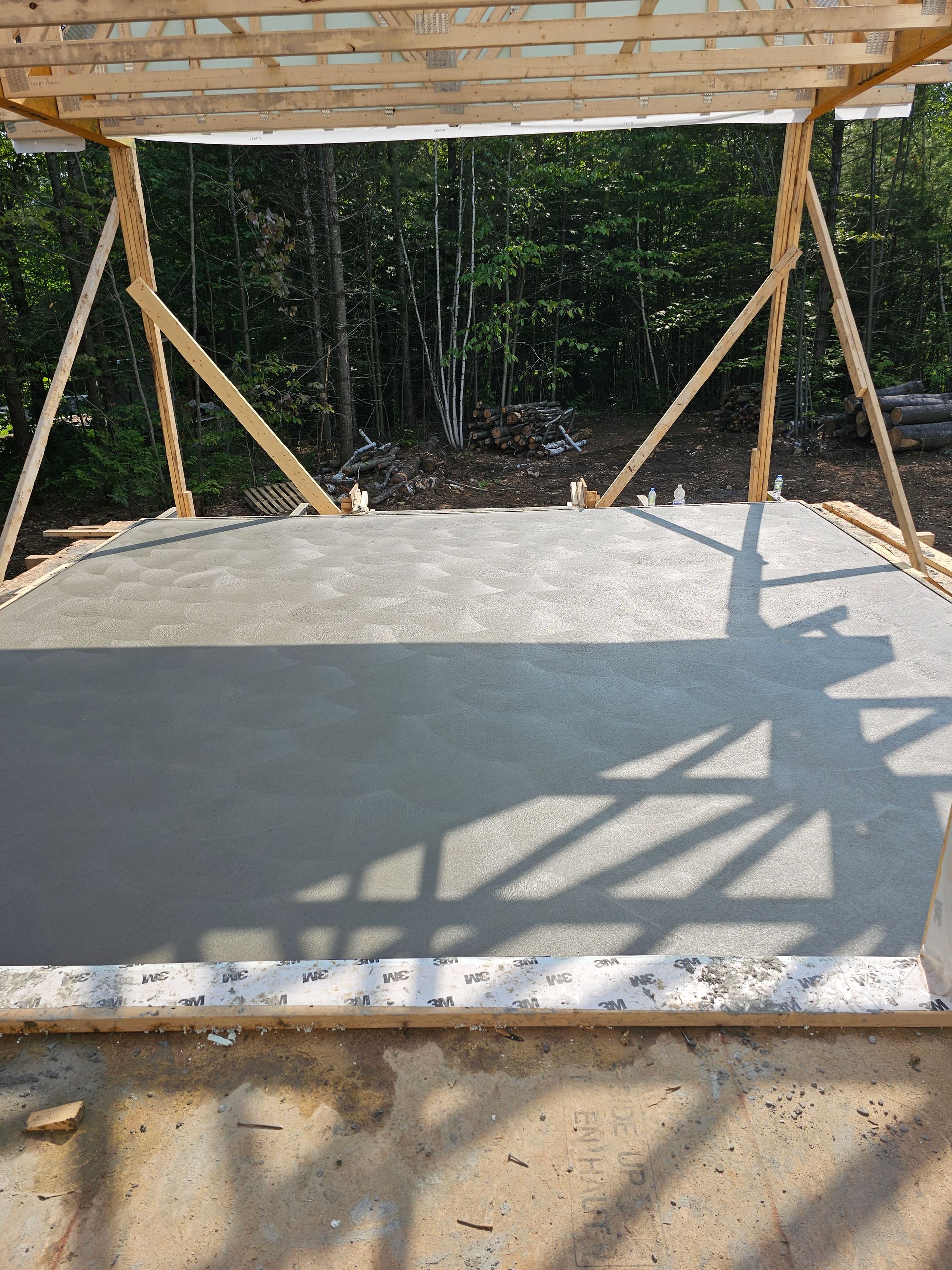Dalle de béton fraîchement coulée avec ossature en bois dans un cadre extérieur boisé.