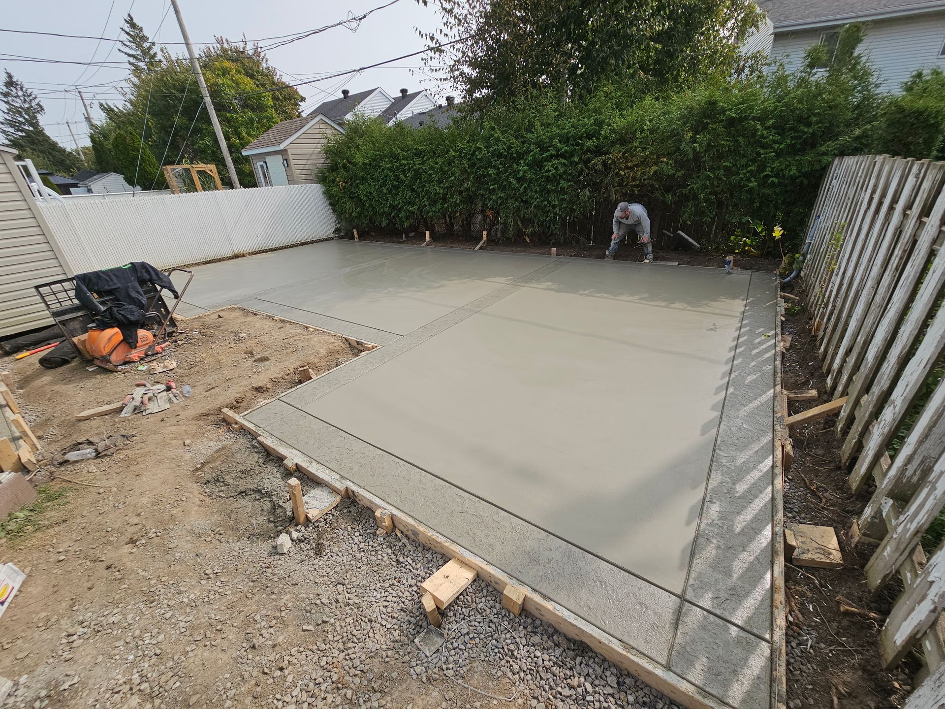 Un homme travaille sur une allée en béton dans une cour arrière.