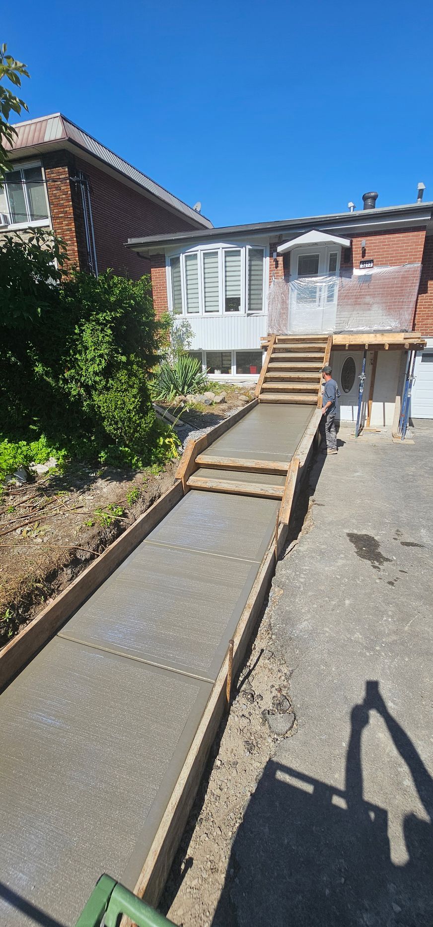 Rampe en béton fraîchement coulée menant à une maison avec des escaliers, sous un ciel bleu.