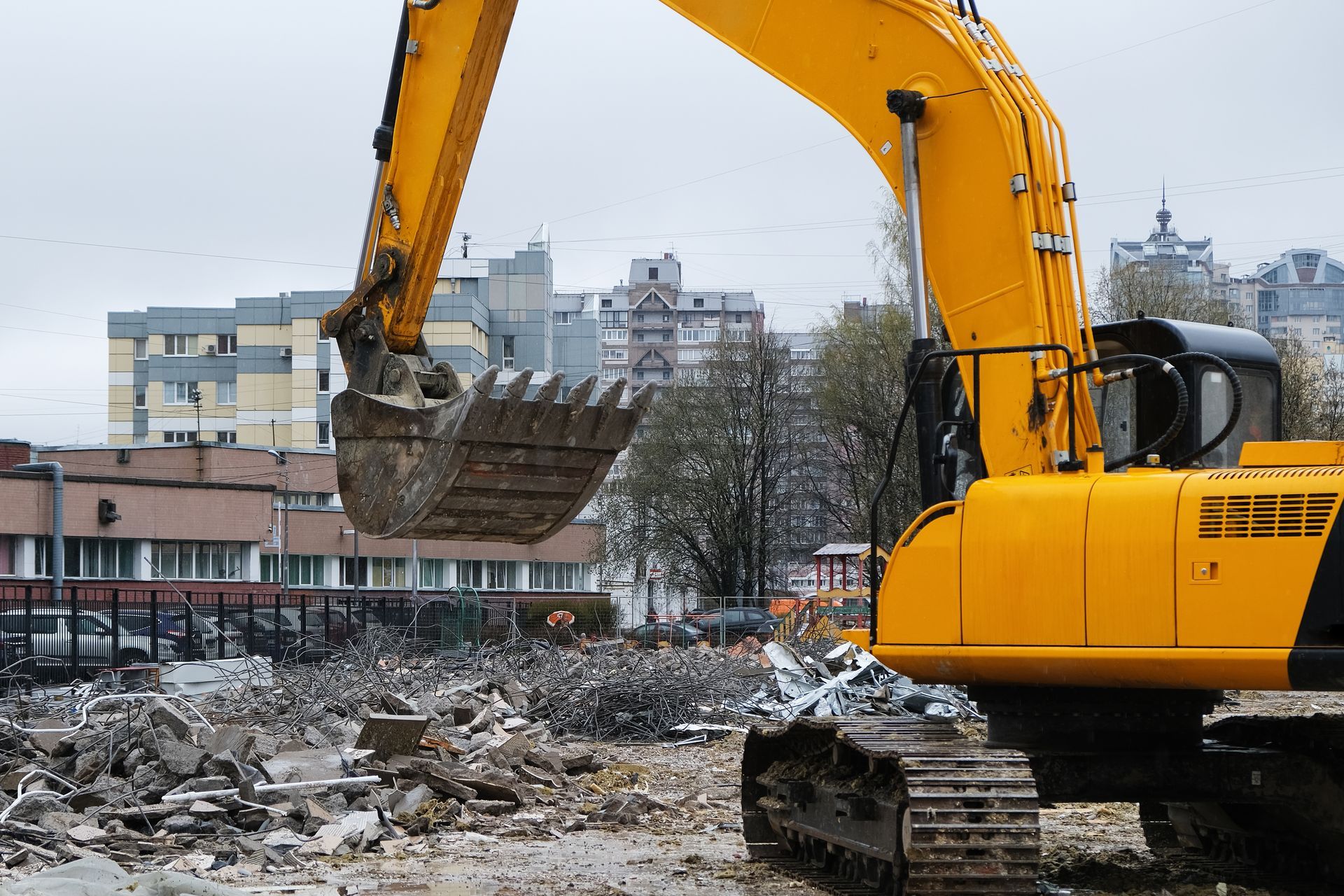 Excavatrice jaune sur un chantier de construction, avec des décombres et des bâtiments en arrière-plan.